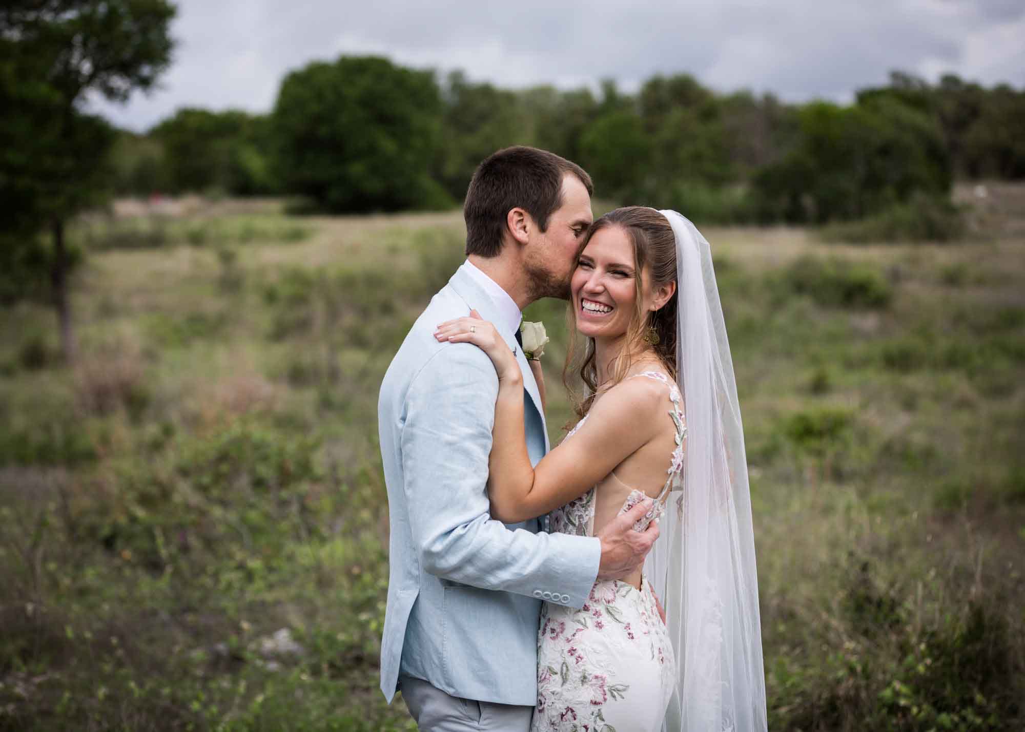 Lady Bird Johnson Wildflower Center wedding photos of a bride and groom hugging and laughing in middle of Savanna Meadow