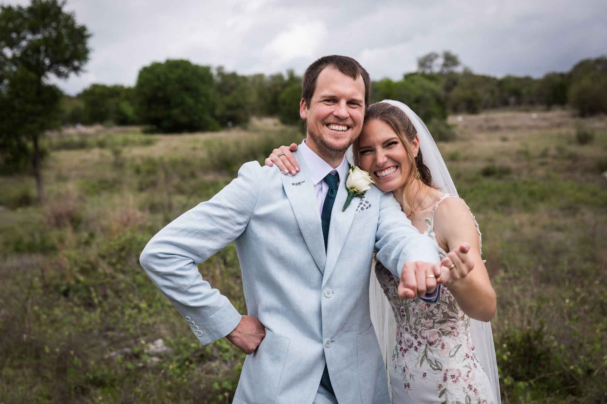 Lady Bird Johnson Wildflower Center wedding photos of a bride and groom laughing and holding out hands showing rings in middle of Savanna Meadow