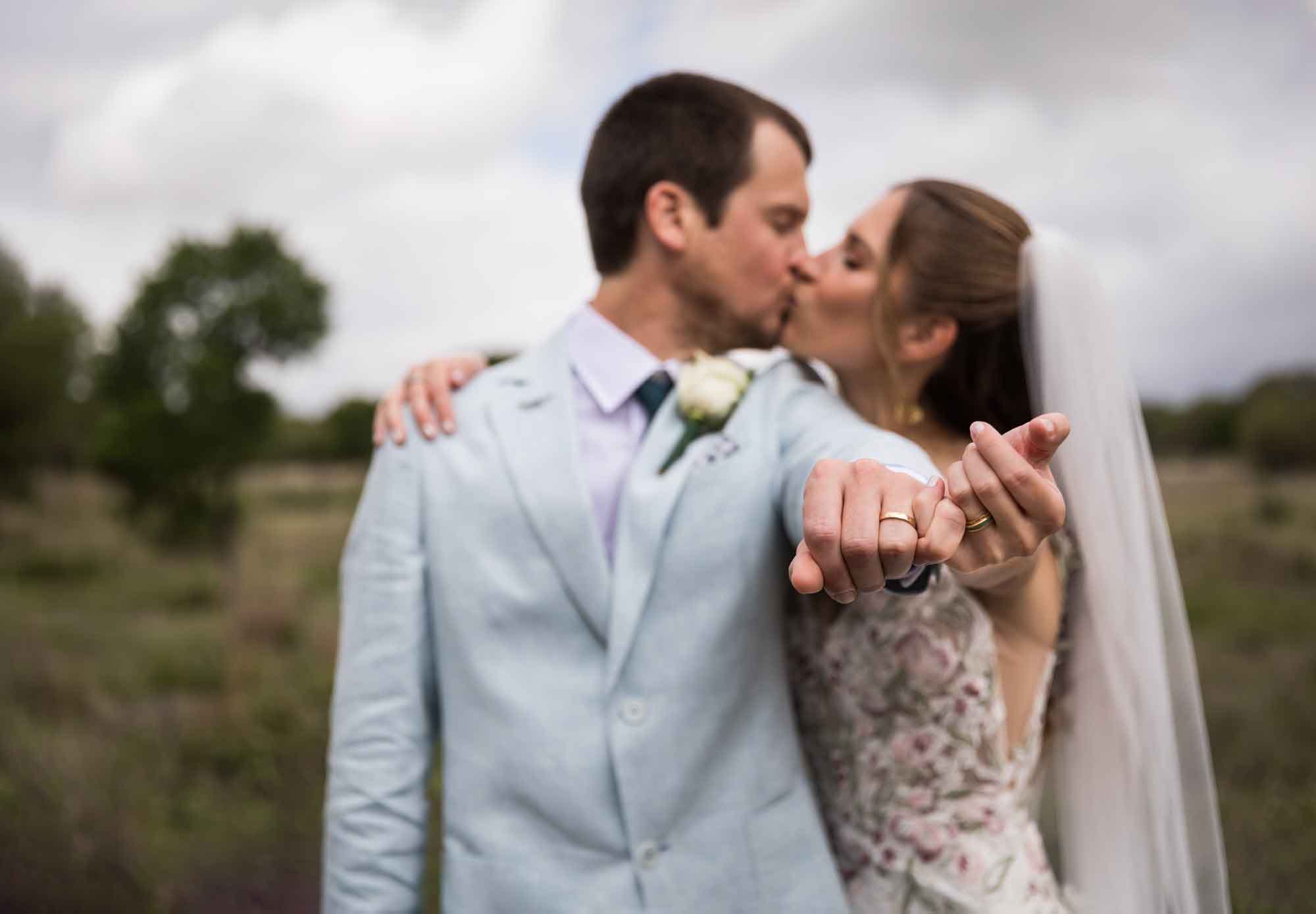 Lady Bird Johnson Wildflower Center wedding photos of a bride and groom kissing and holding out hands showing rings in middle of Savanna Meadow