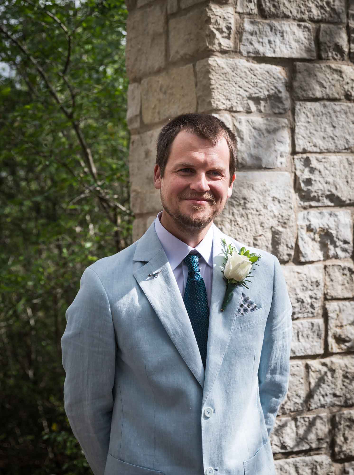 Groom wearing light blue blazer and white rose in front of Cecille's Arch during a Lady Bird Johnson Wildflower Center wedding