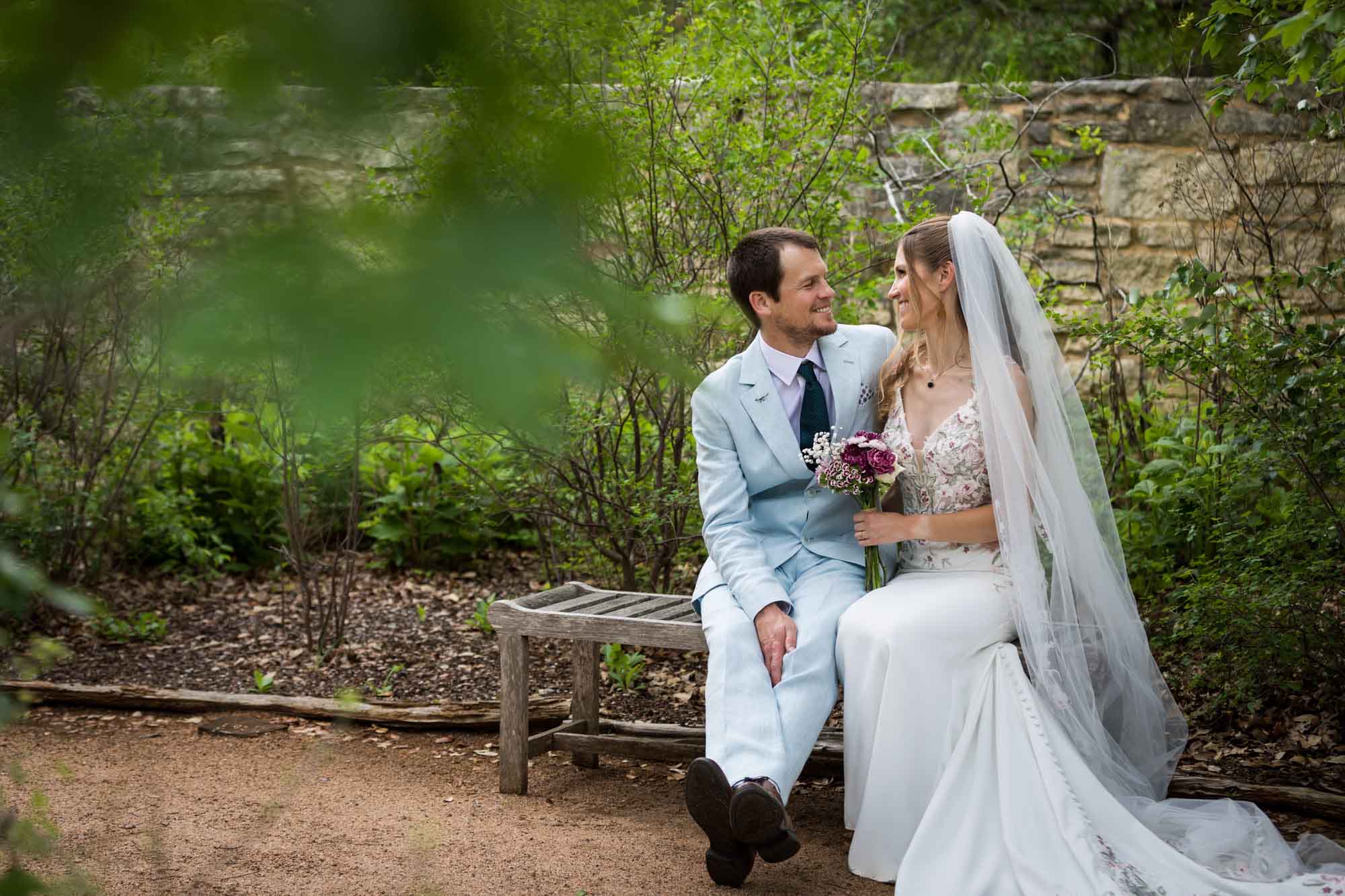 Lady Bird Johnson Wildflower Center wedding photos of a bride and groom sitting on bench laughing