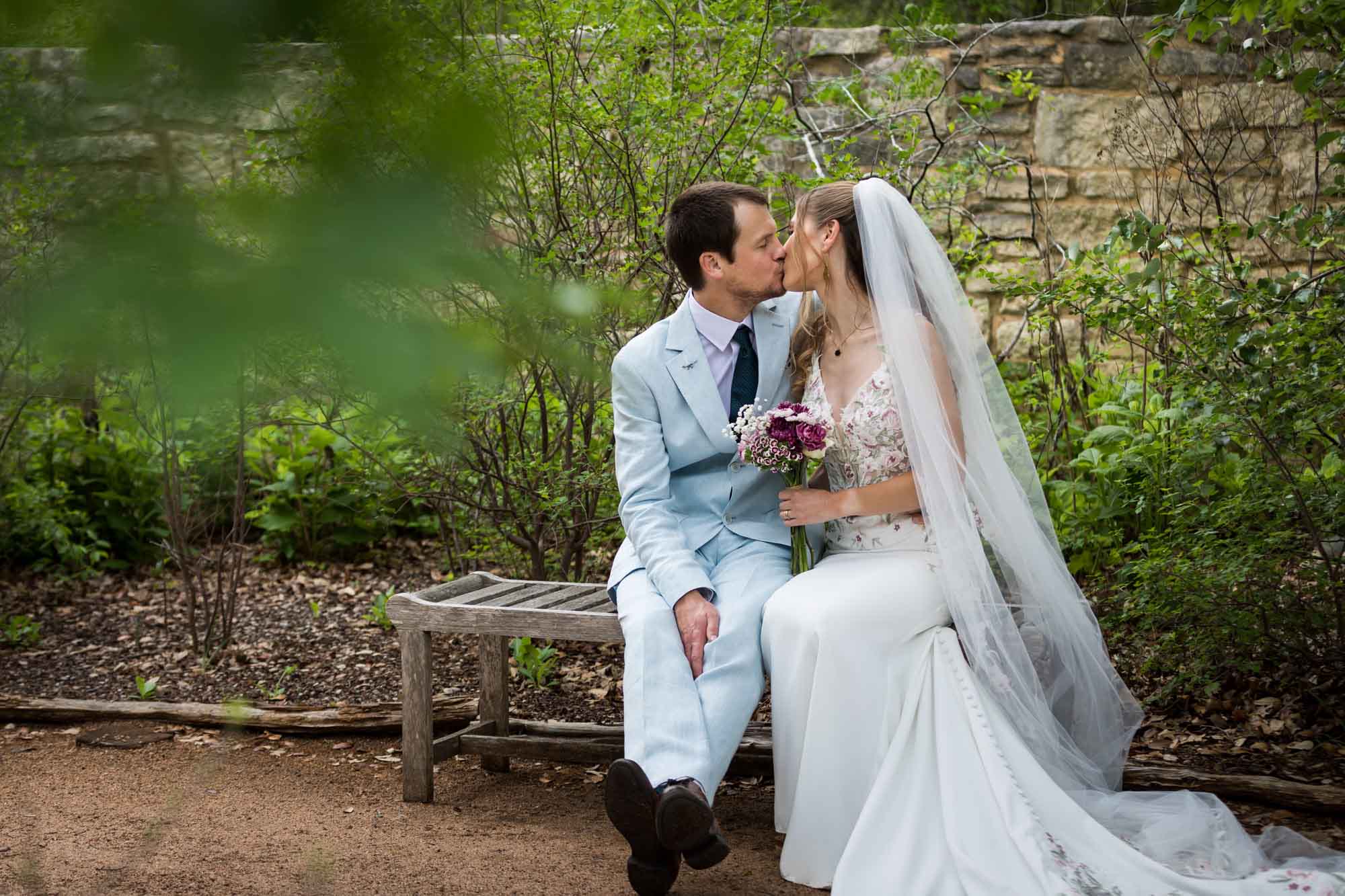 Lady Bird Johnson Wildflower Center wedding photos of a bride and groom sitting on bench kissing
