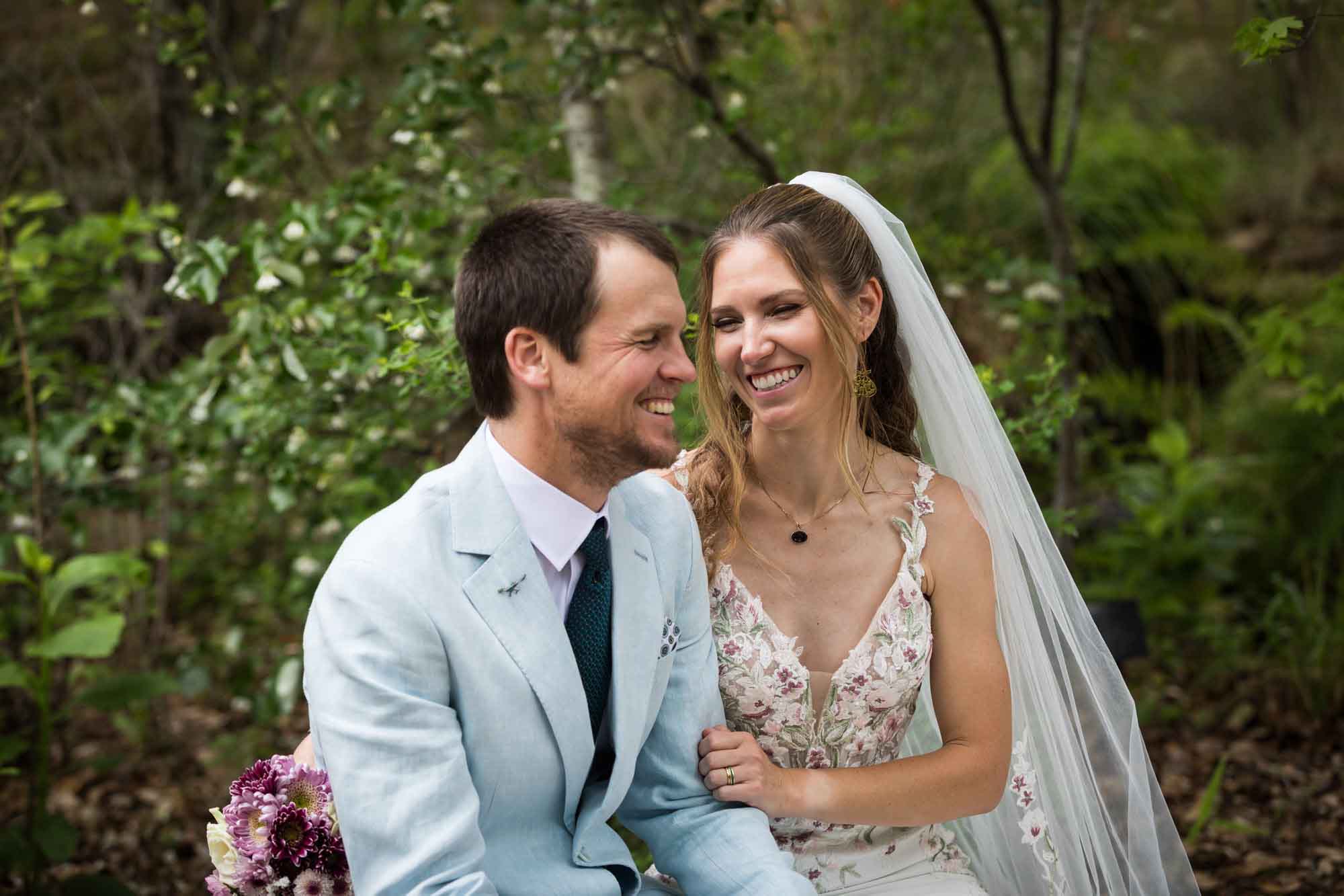 Lady Bird Johnson Wildflower Center wedding photos of a bride and groom sitting on bench laughing