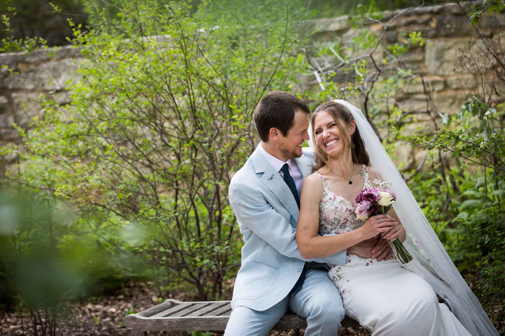 Lady Bird Johnson Wildflower Center wedding photos of a bride and groom sitting on bench laughing