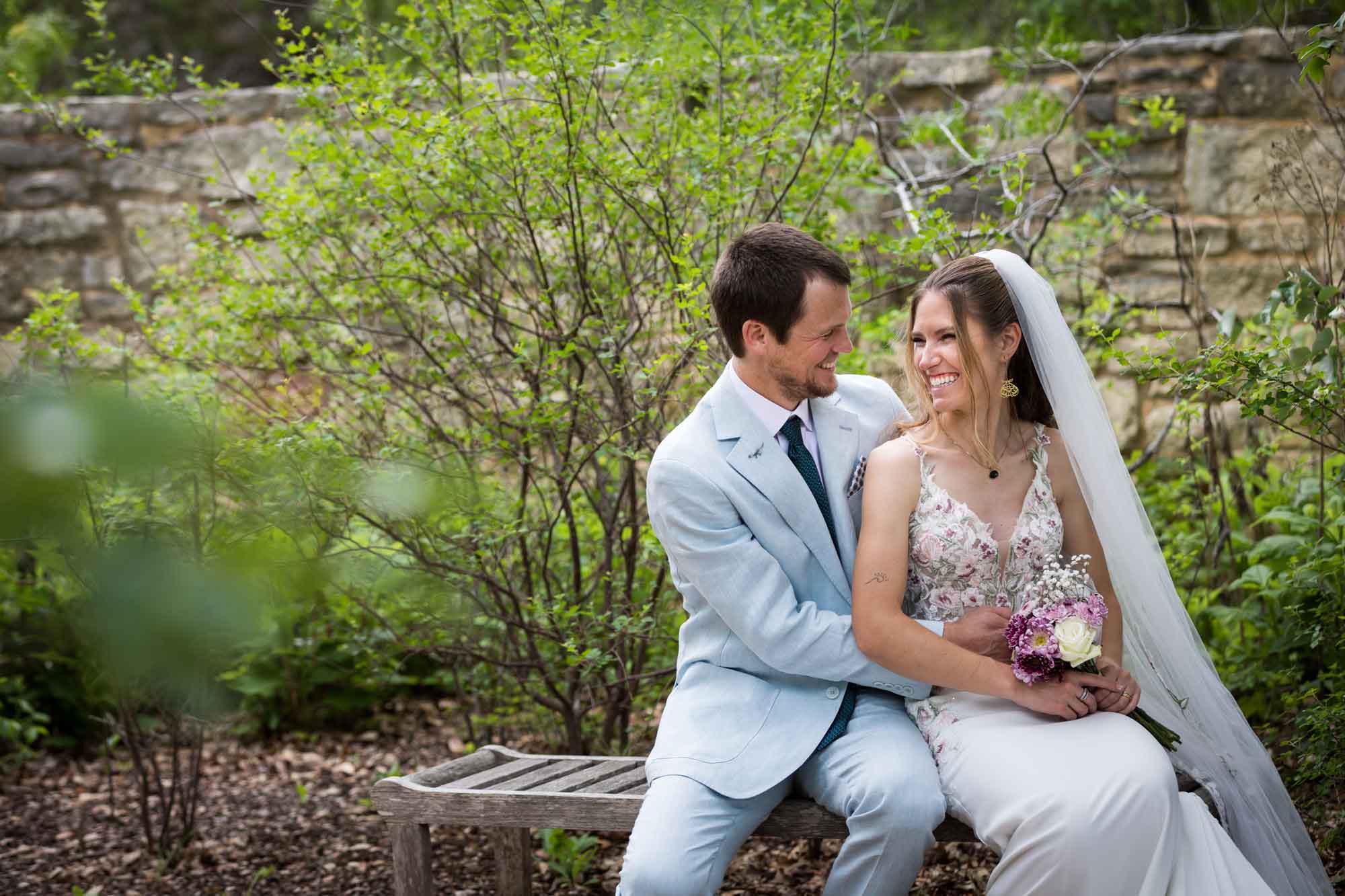 Lady Bird Johnson Wildflower Center wedding photos of a bride and groom sitting on bench laughing