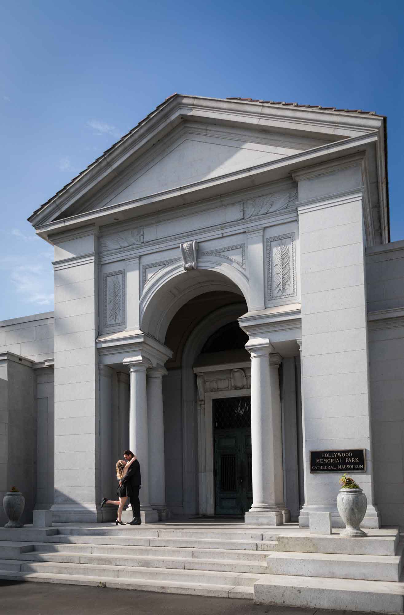Man and woman kissing passionately outside Cathedral Mausoleum during a Hollywood Forever Cemetery engagement portrait session