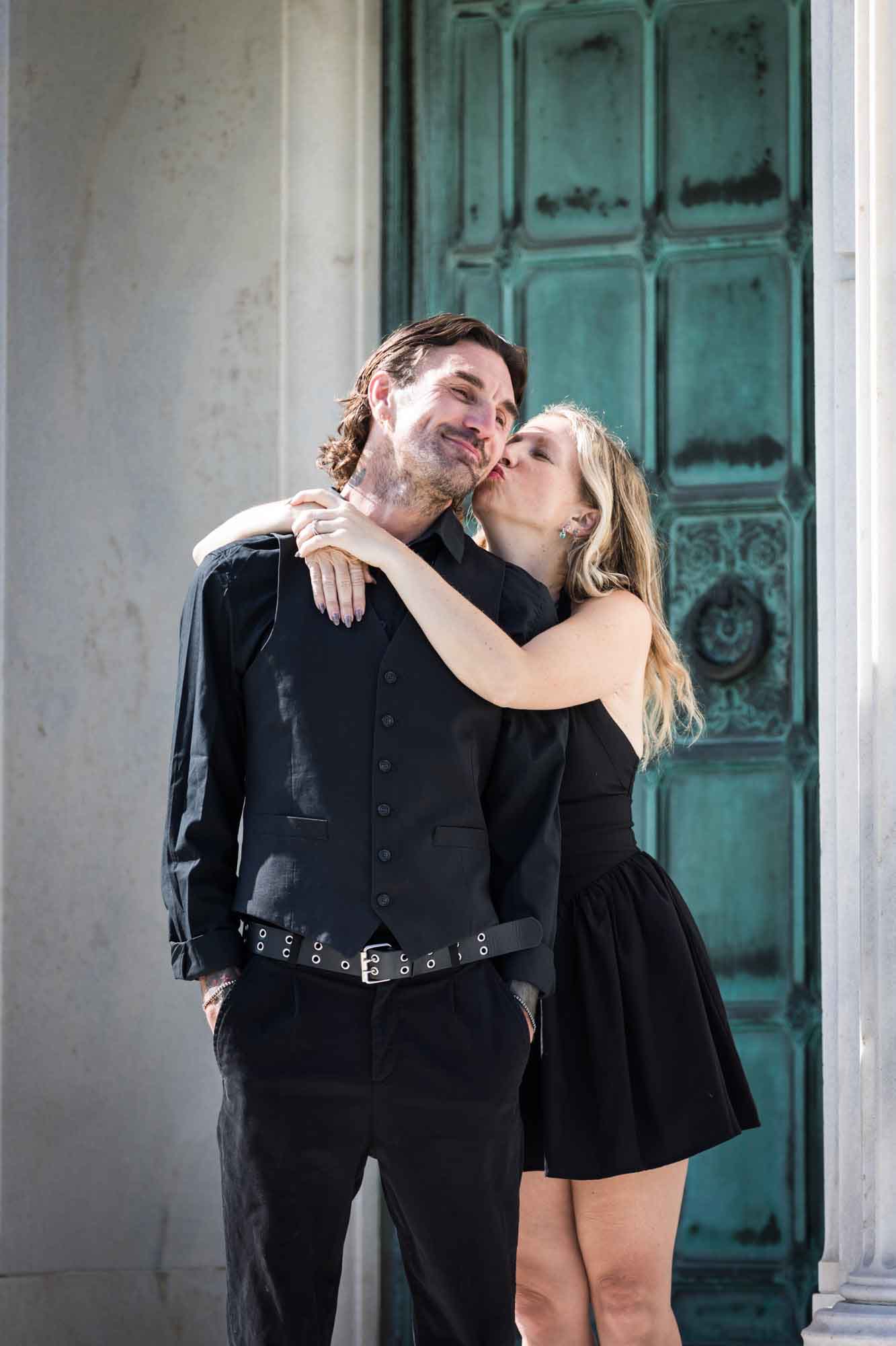 Hollywood Forever Cemetery engagement portrait of woman kissing man on the cheek in front of green door