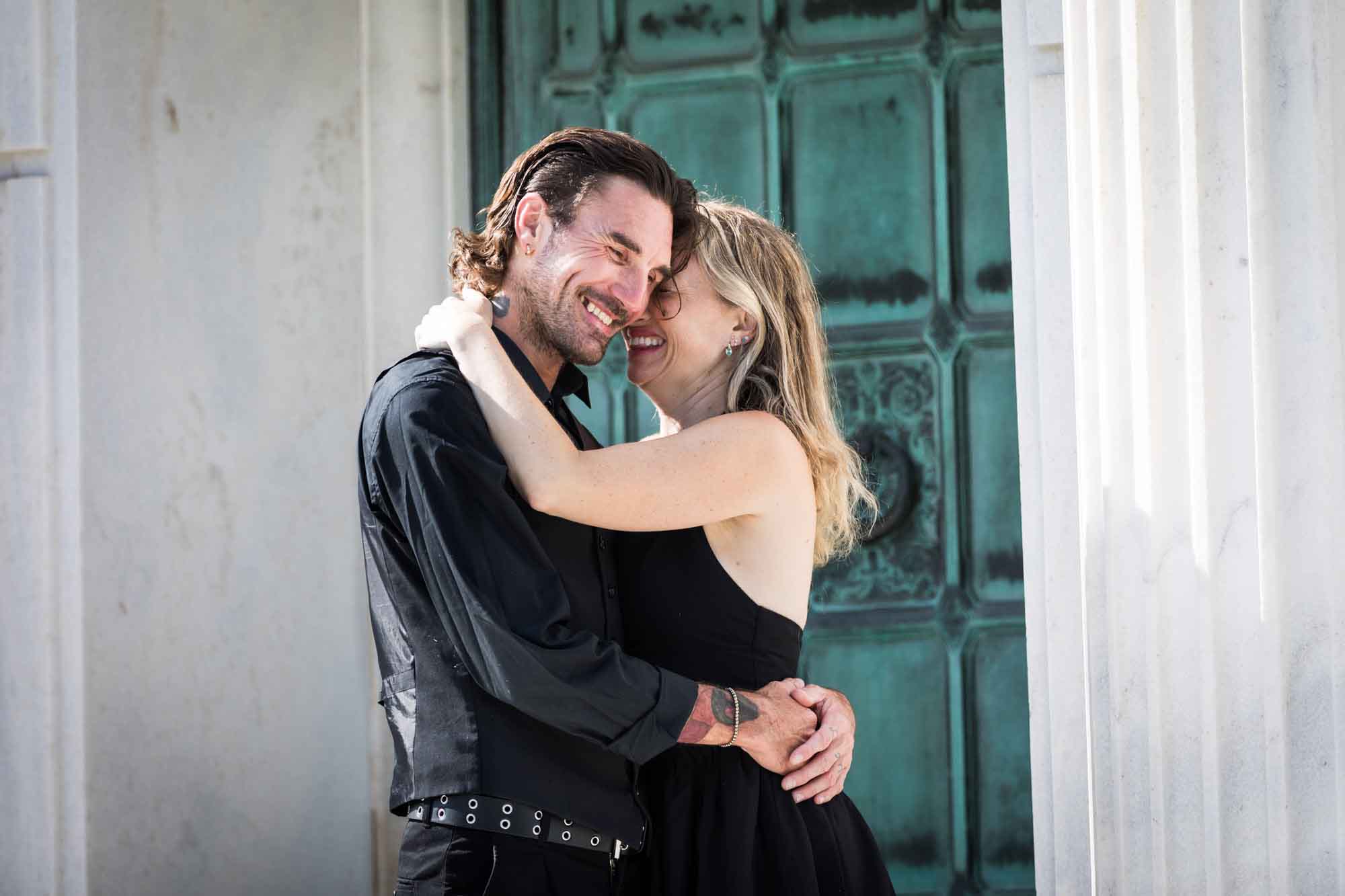Man and woman hugging outside green door during a Hollywood Forever Cemetery engagement portrait session