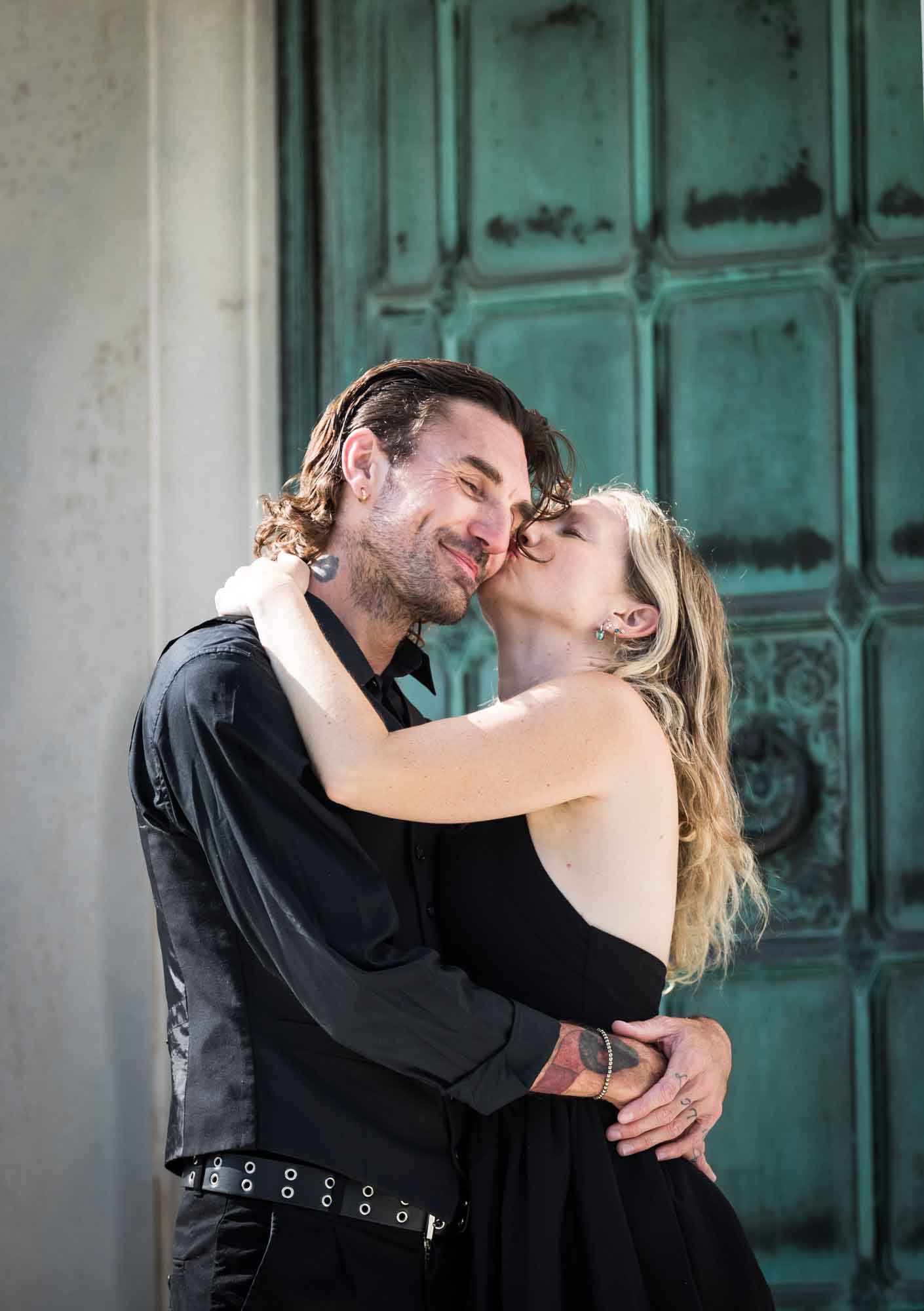 Hollywood Forever Cemetery engagement portrait of woman kissing man on the cheek in front of green door