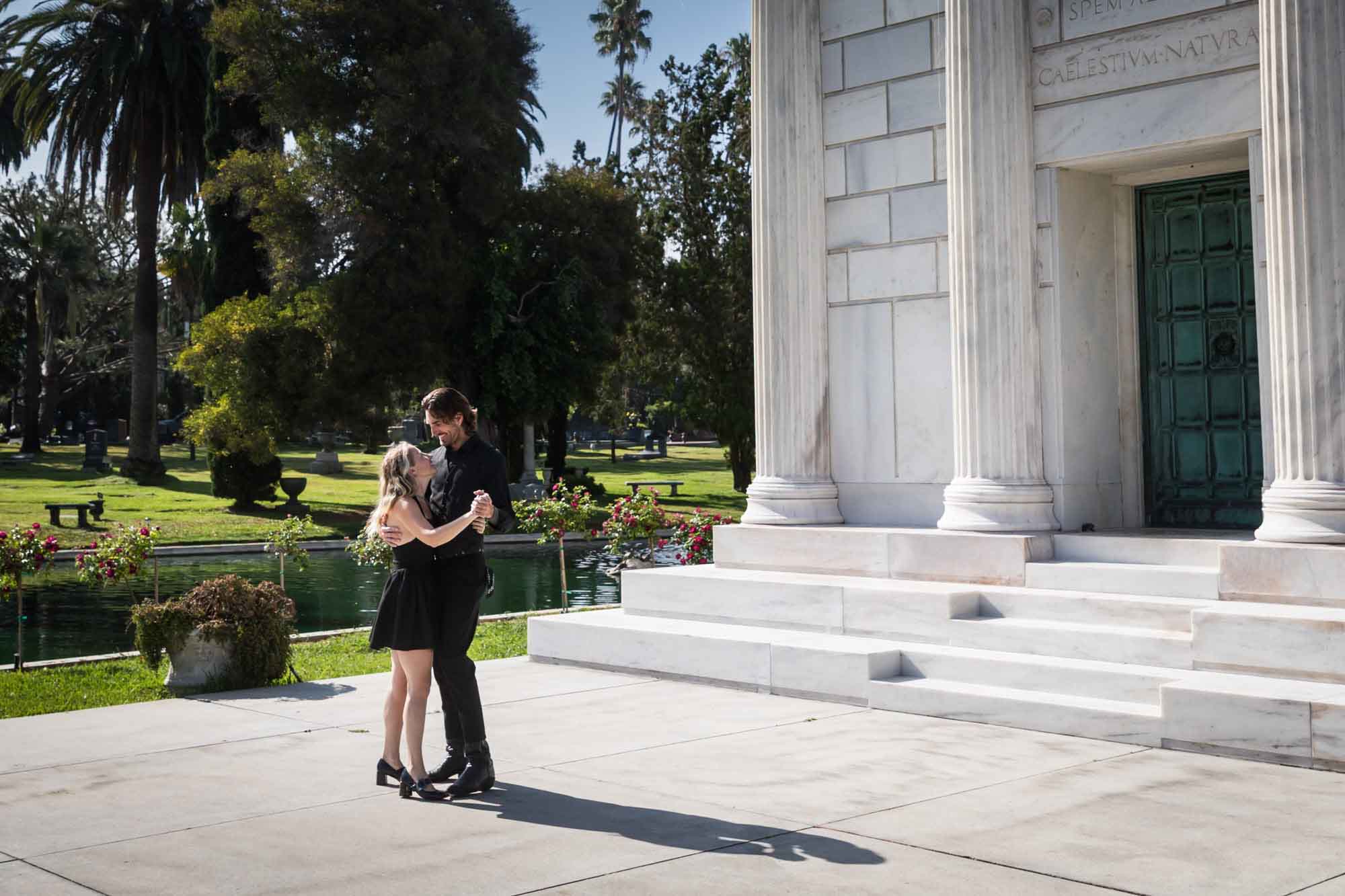 Hollywood Forever Cemetery engagement portrait of man and woman dancing in front of Clark Mausoleum and lake
