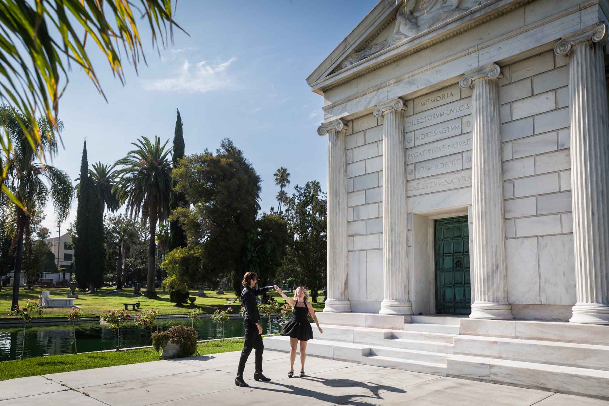 Hollywood Forever Cemetery engagement portrait of man and woman dancing in front of Clark Mausoleum and lake