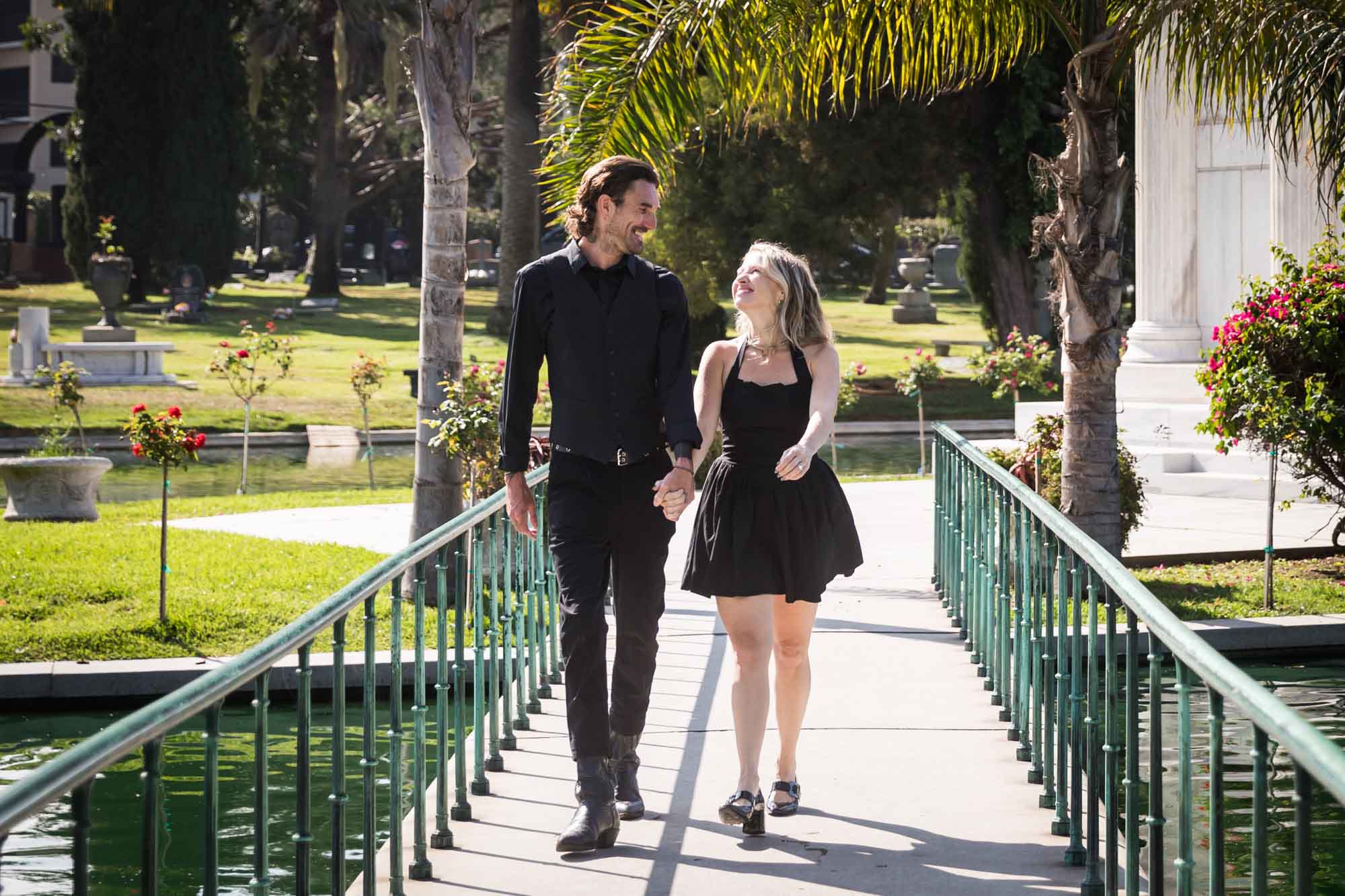 Hollywood Forever Cemetery engagement portrait of man and woman walking down pathway with Clark Mausoleum and lake in background
