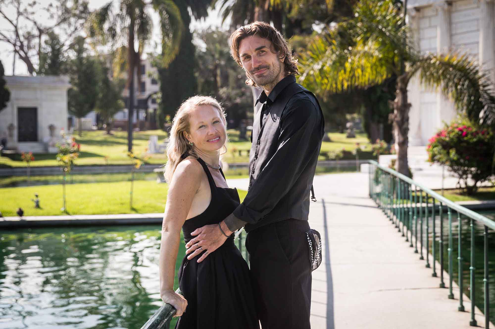 Hollywood Forever Cemetery engagement portrait of man and woman leaning against railing with lake in background