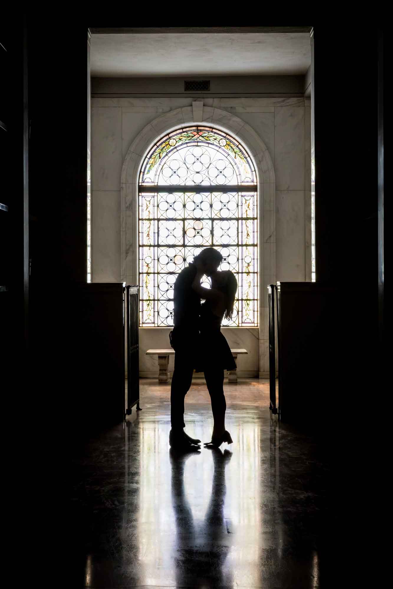 Hollywood Forever Cemetery engagement portrait of man and woman kissing in front of stained glass window in Cathedral Mausoleum