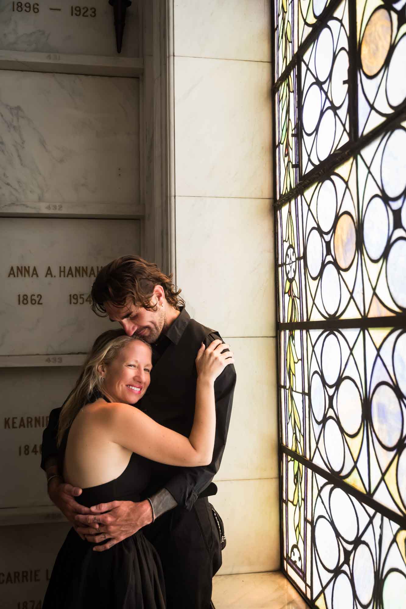 Hollywood Forever Cemetery engagement portrait of man and woman hugging in front of stained glass window in Cathedral Mausoleum