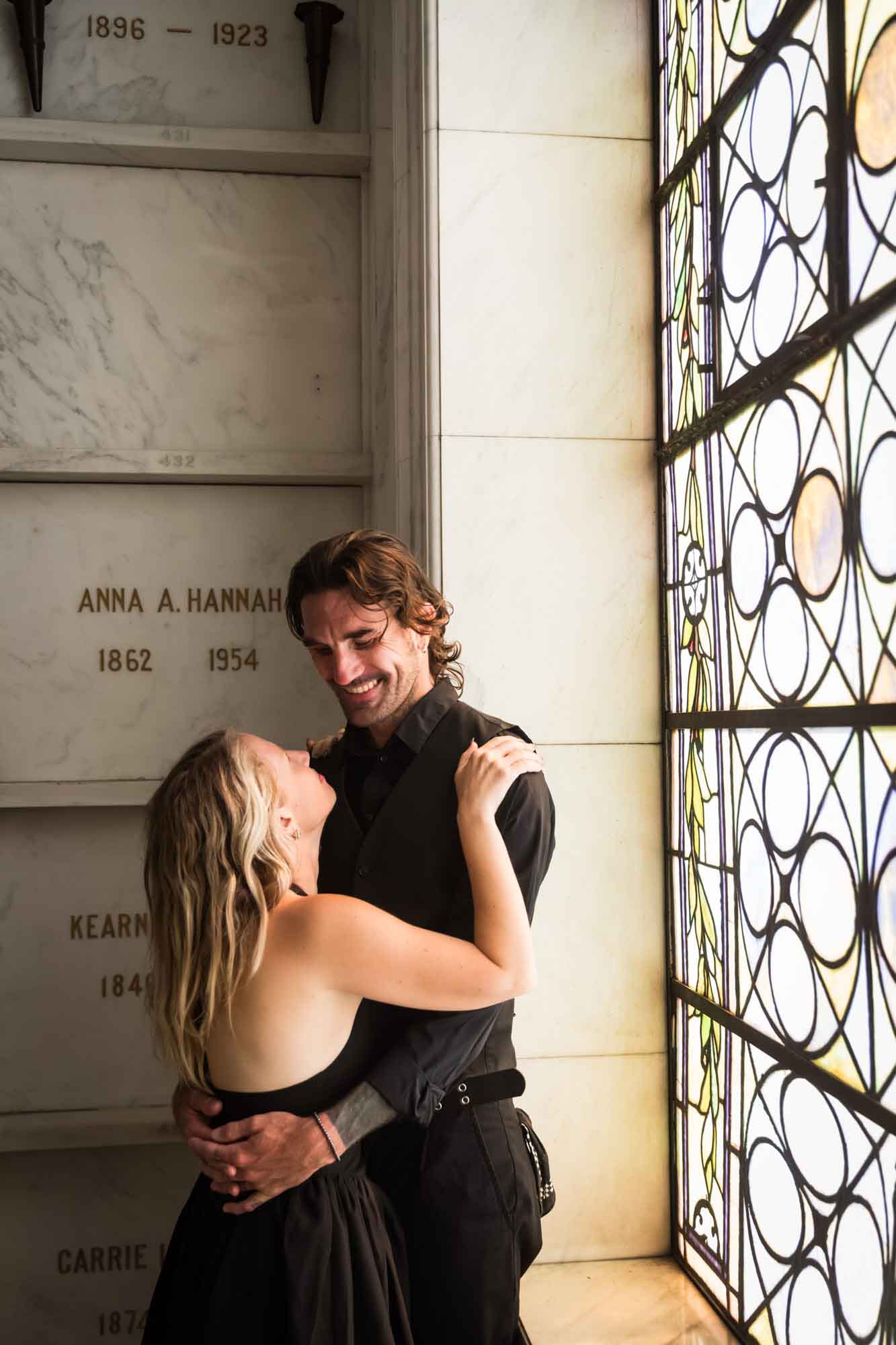 Hollywood Forever Cemetery engagement portrait of man and woman hugging in front of stained glass window in Cathedral Mausoleum