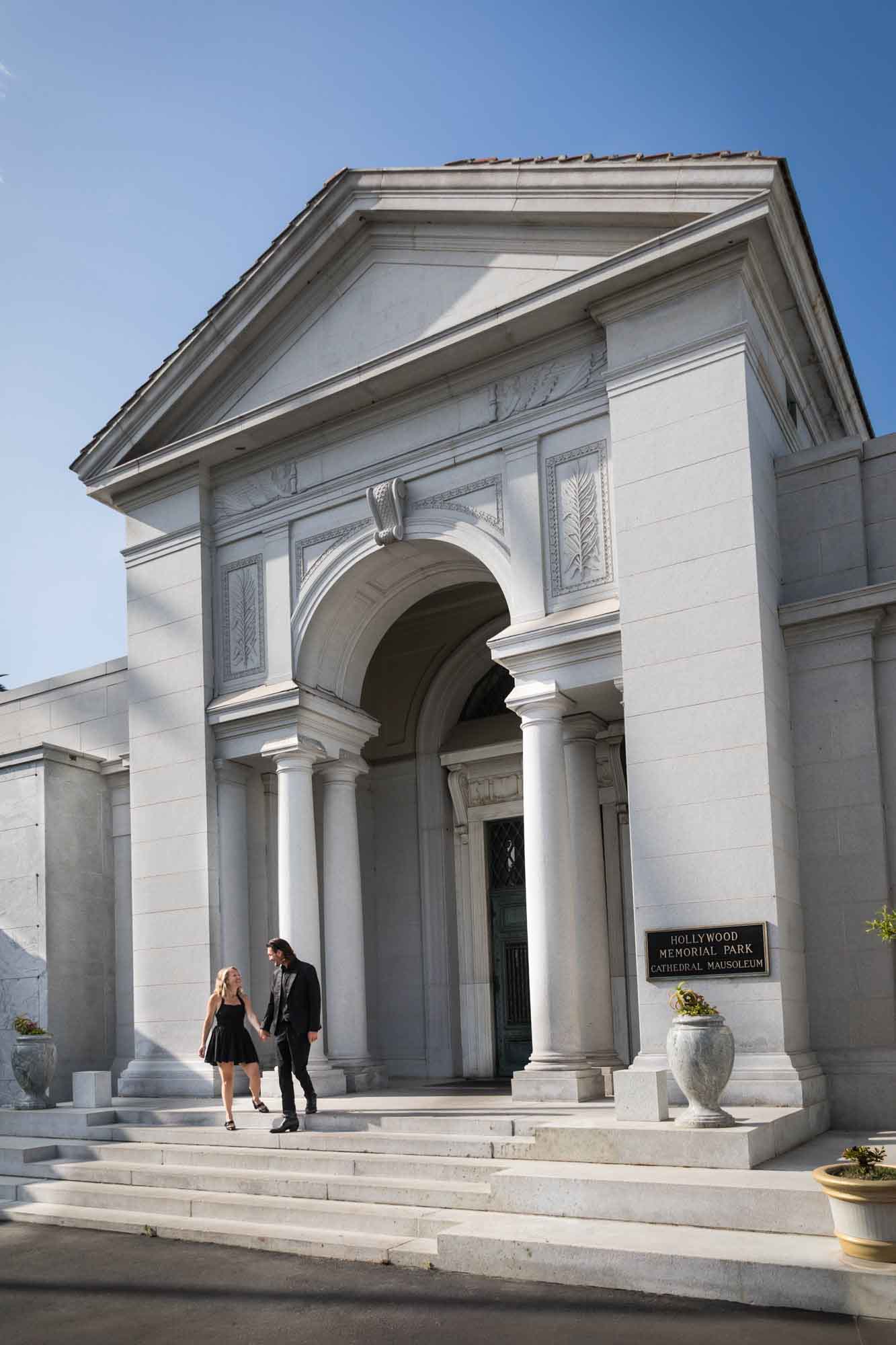 Man and woman walking down steps outside Cathedral Mausoleum during a Hollywood Forever Cemetery engagement portrait session
