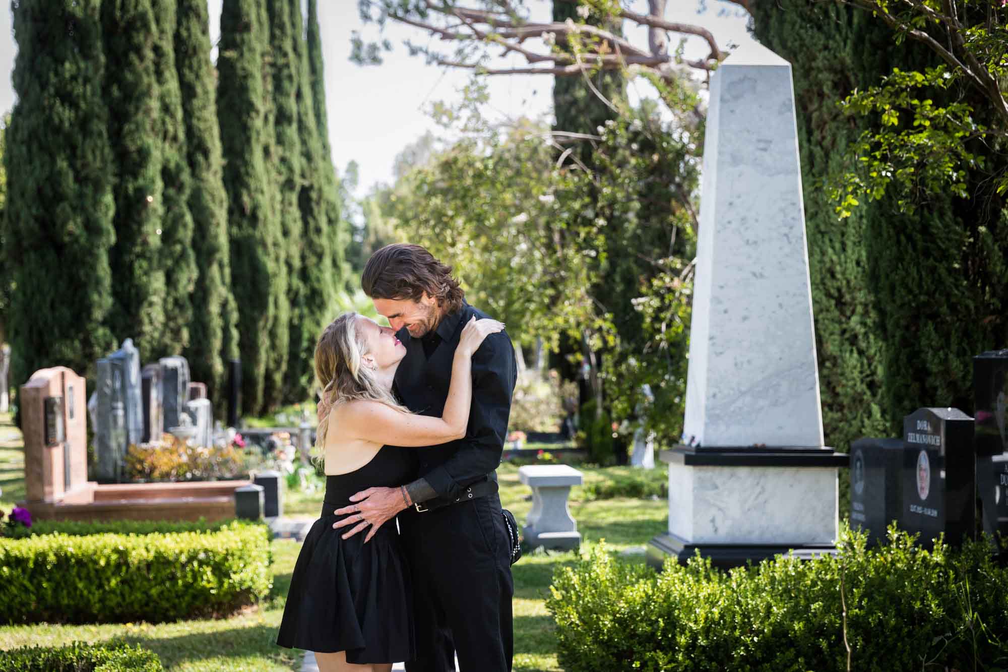 Man and woman looking at each other and hugging in Ancestral Forest walkway during a Hollywood Forever Cemetery engagement portrait session