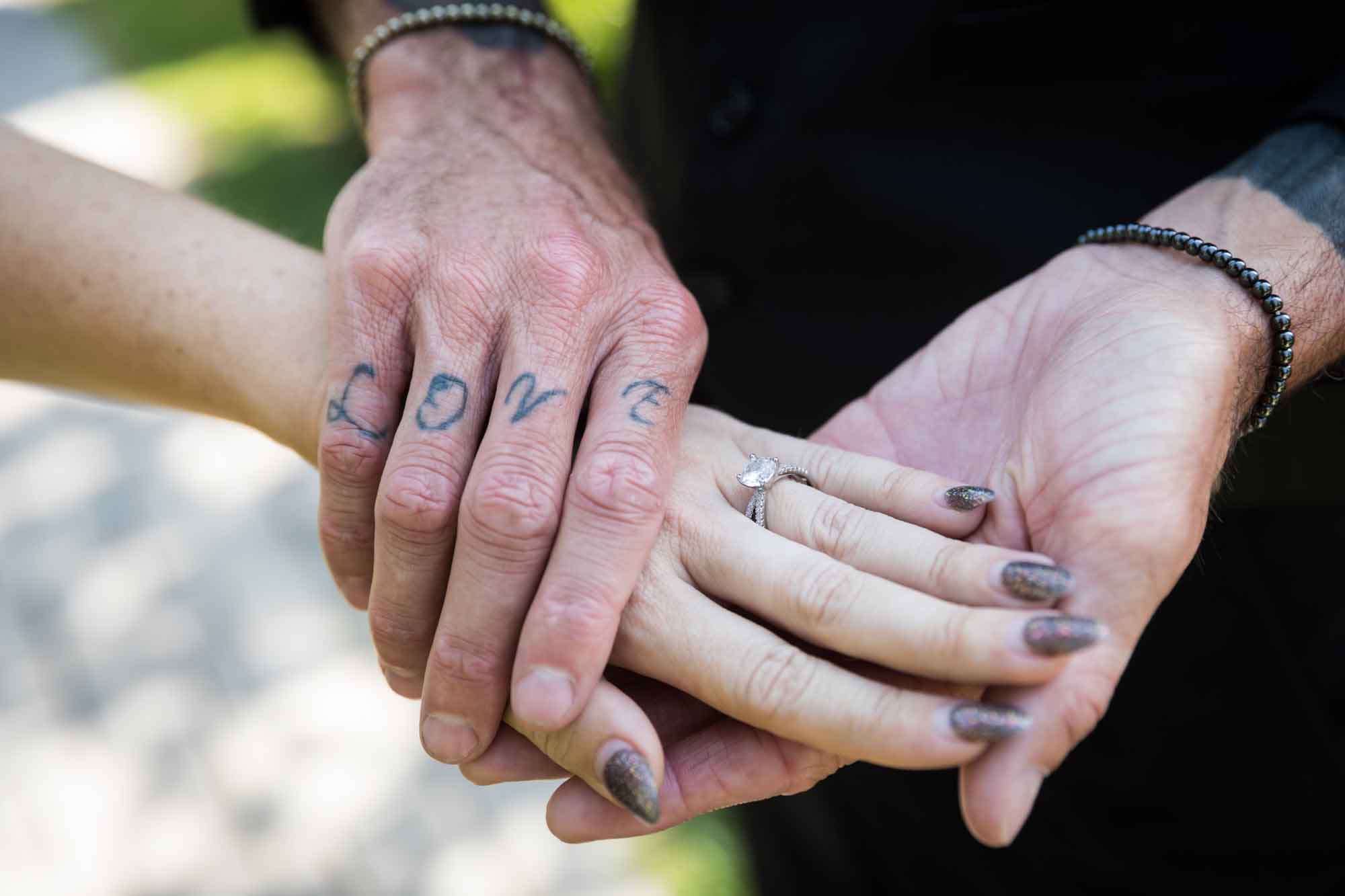Close up of man holding woman's hand showing engagement ring with man's hand tattooed with the word 'love' during a Hollywood Forever Cemetery engagement portrait session