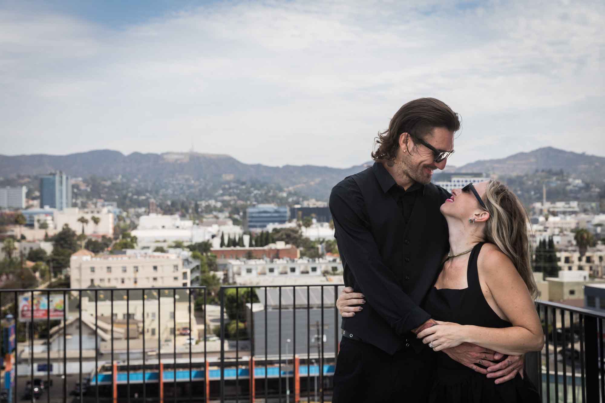 Man and woman hugging in front of Los Angeles skyline on rooftop during a Hollywood Forever Cemetery engagement portrait session