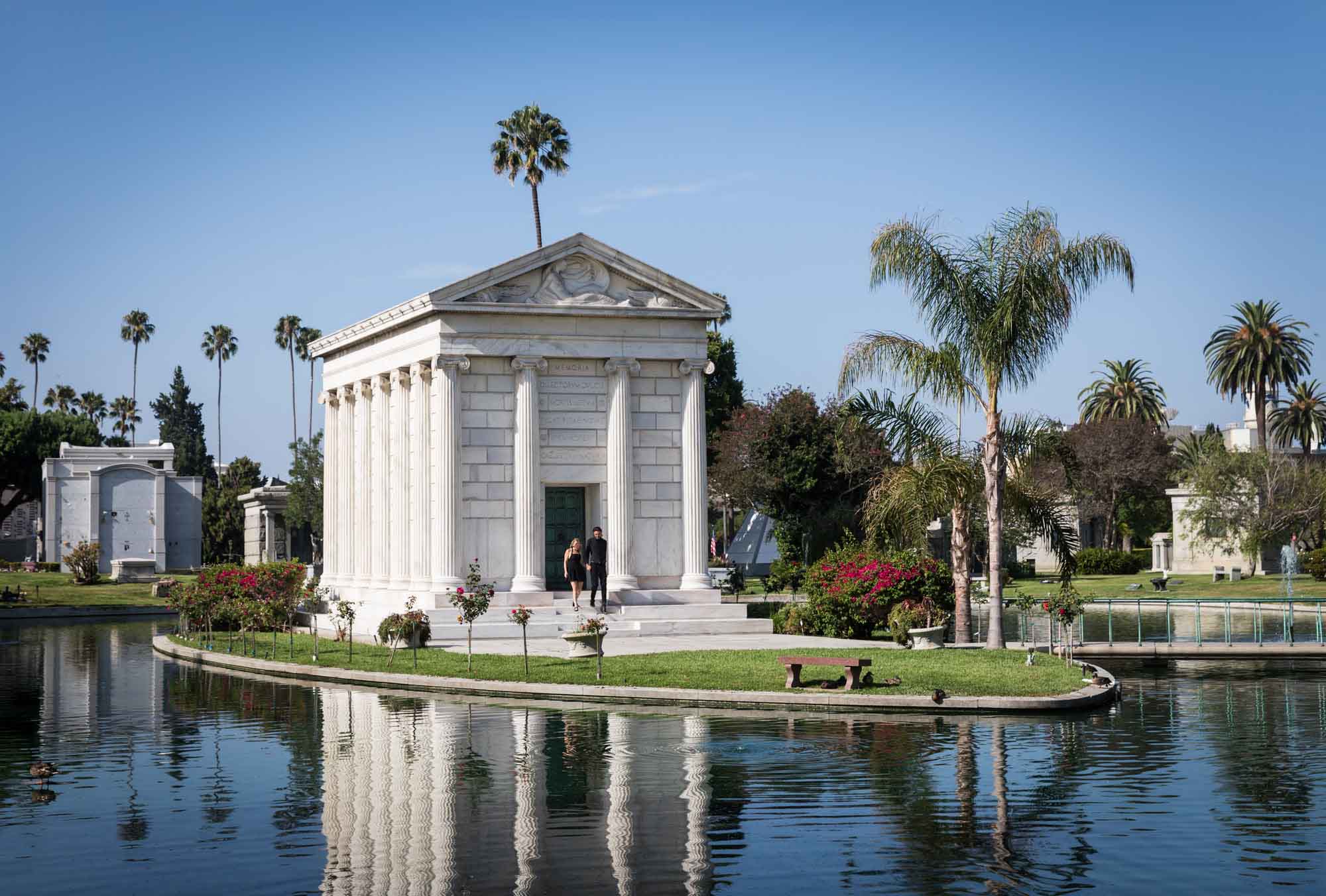 Hollywood Forever Cemetery engagement portrait of man and woman walking down steps of the Clark Mausoleum in middle of lake