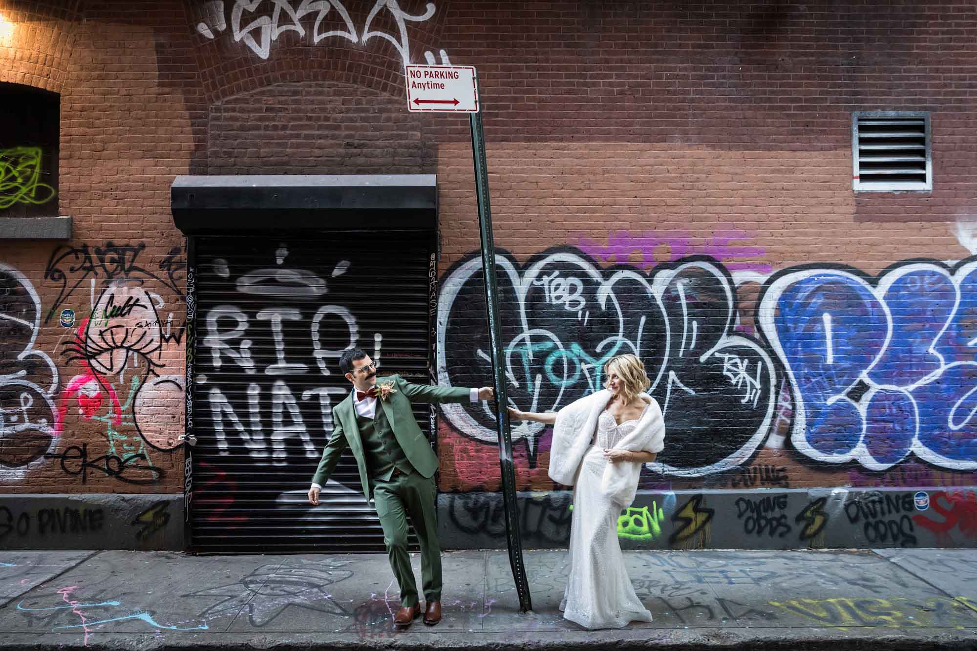 Bride and groom hanging from street sign in middle of street with graffiti-covered walls in background for an article on how to get a marriage license in Los Angeles