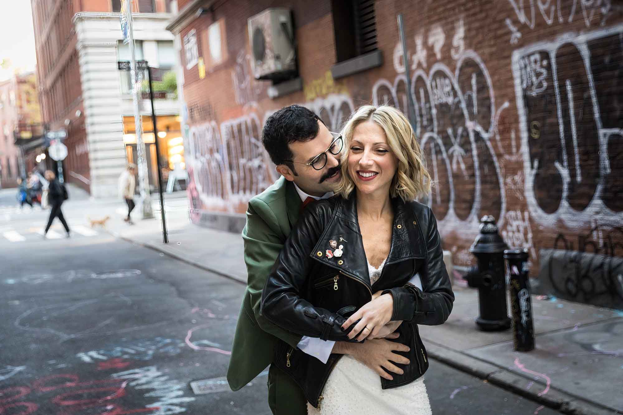 Groom kissing bride with hug from behind in middle of street with graffiti covered walls in background for an article on how to get a marriage license in Los Angeles