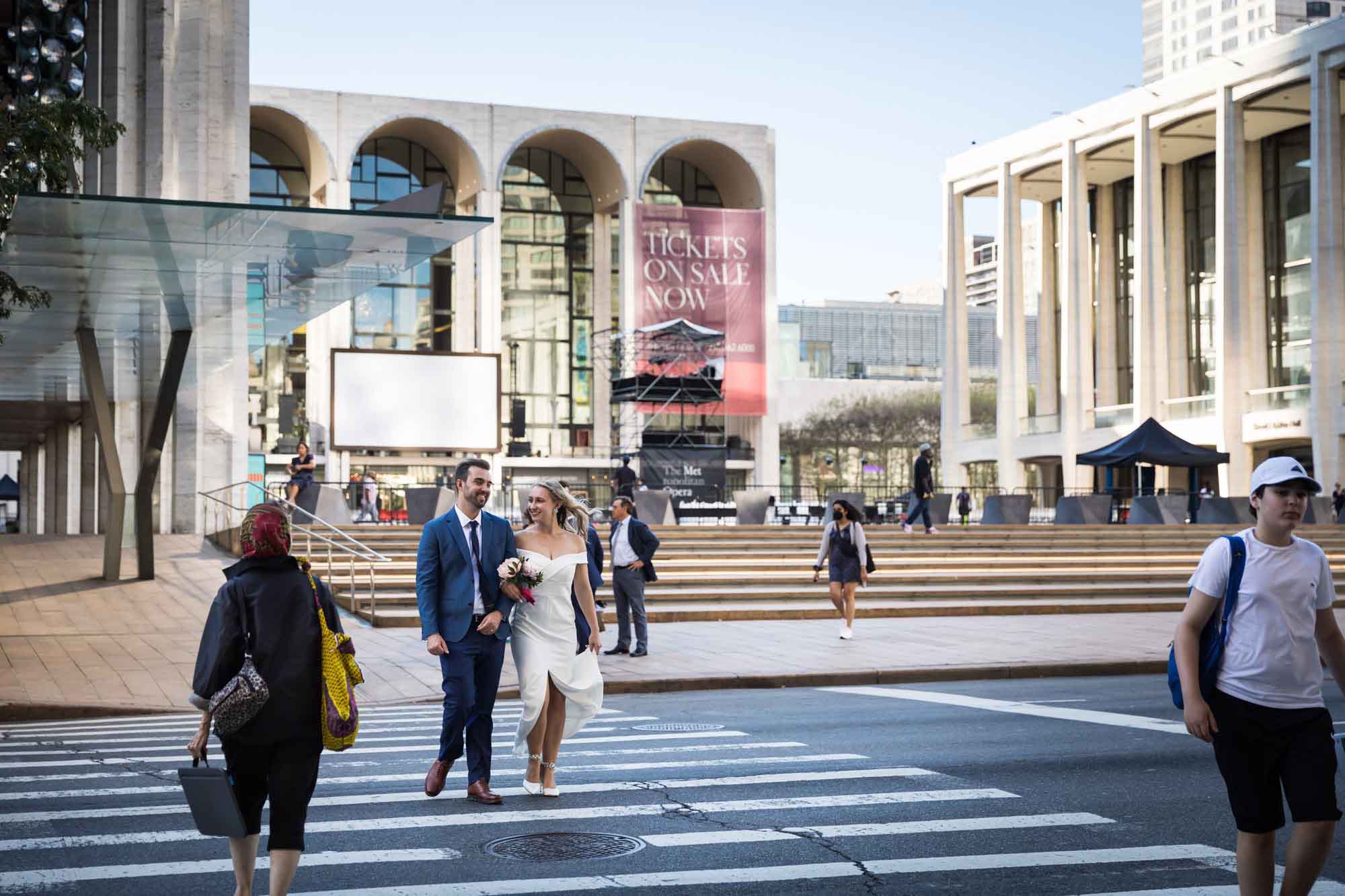 Bride and groom walking hand in hand in crosswalk in front of Lincoln Center for an article on how to get a marriage license in Los Angeles