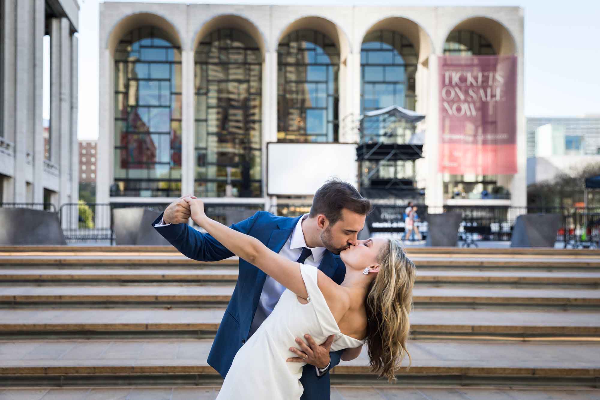 Bride and groom kissing with flair with Lincoln Center and stairs in background for an article on how to get a marriage license in Los Angeles