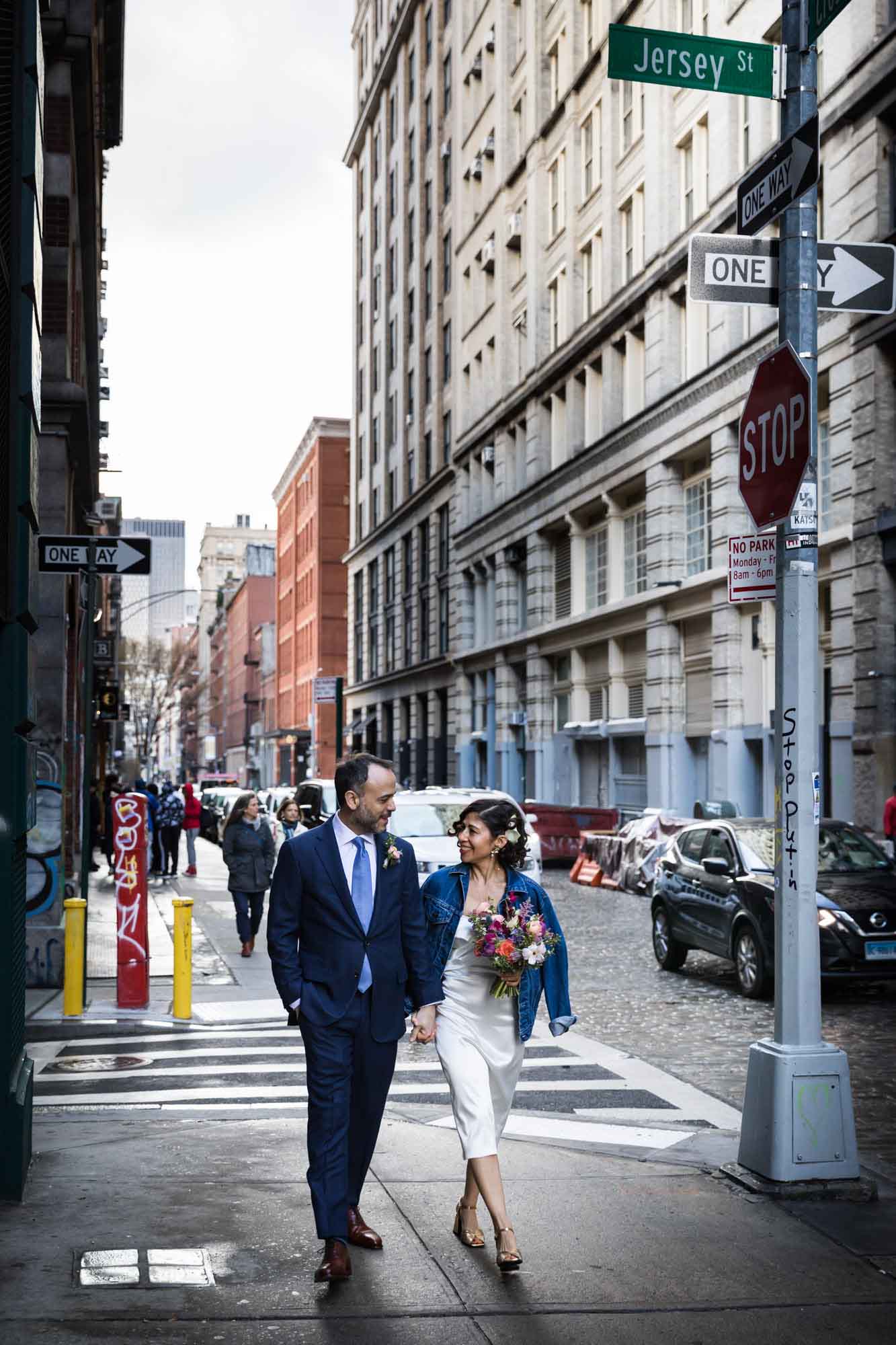 Bride and groom walking down sidewalk with large buildings and traffic in the background for an article on how to get a marriage license in Los Angeles