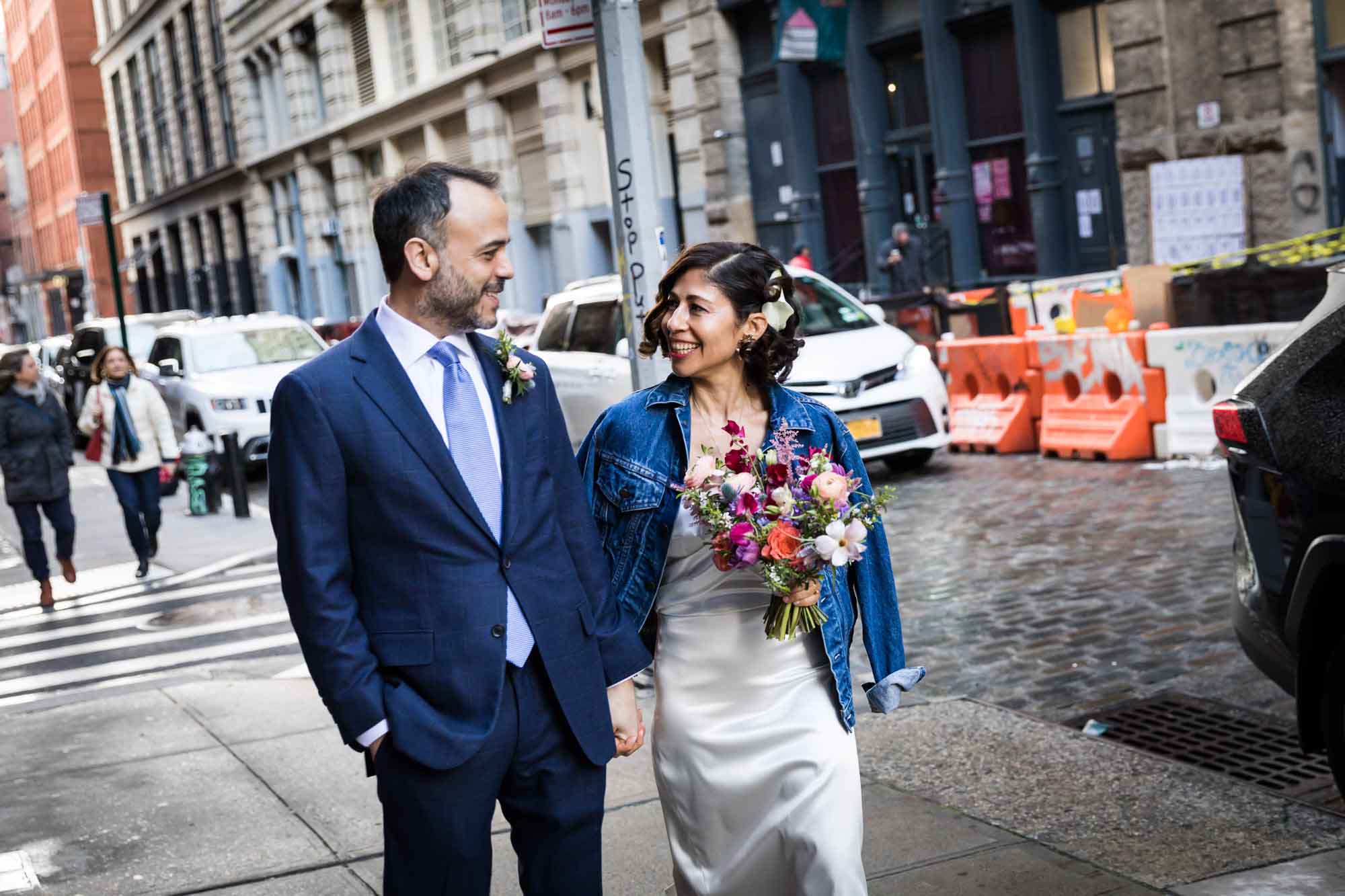 Bride and groom walking down city sidewalk with traffic in the background for an article on how to get a marriage license in Los Angeles