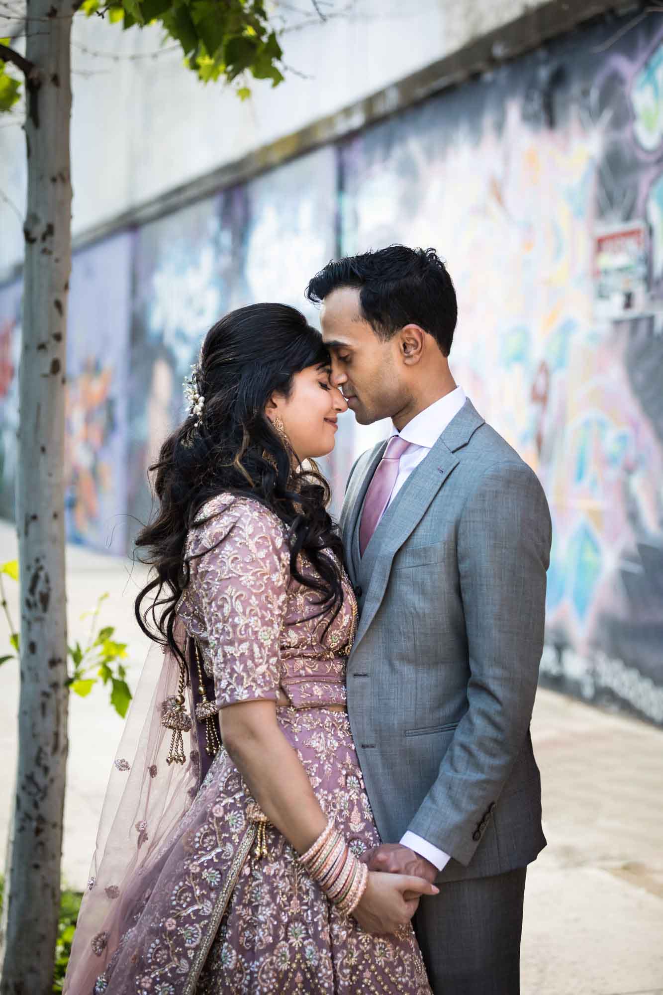 Indian bride and groom holding hands and touching foreheads with graffiti walls in background for an article on how to get a marriage license in Los Angeles