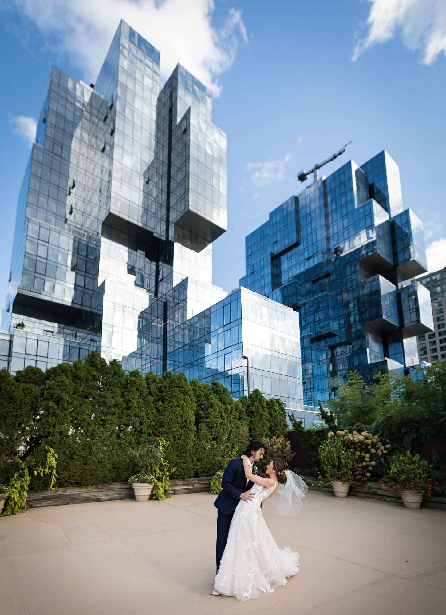Bride and groom dancing in front of large skyscraper with mirrored exterior showing clouds for an article on how to get a marriage license in Los Angeles