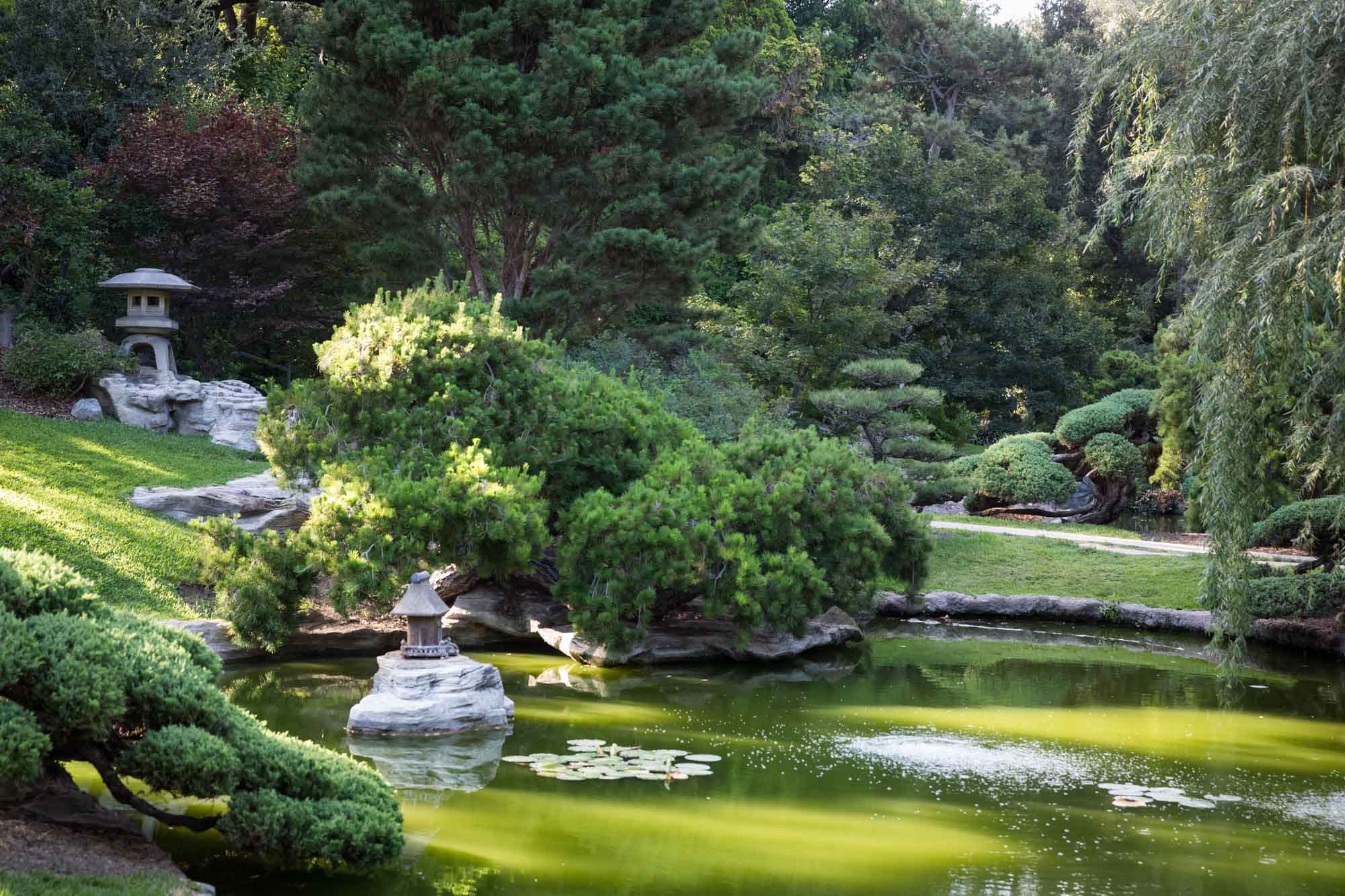 Stone lanterns and bushes across from pond in Japanese Garden for a Huntington Gardens photo shoot guide article