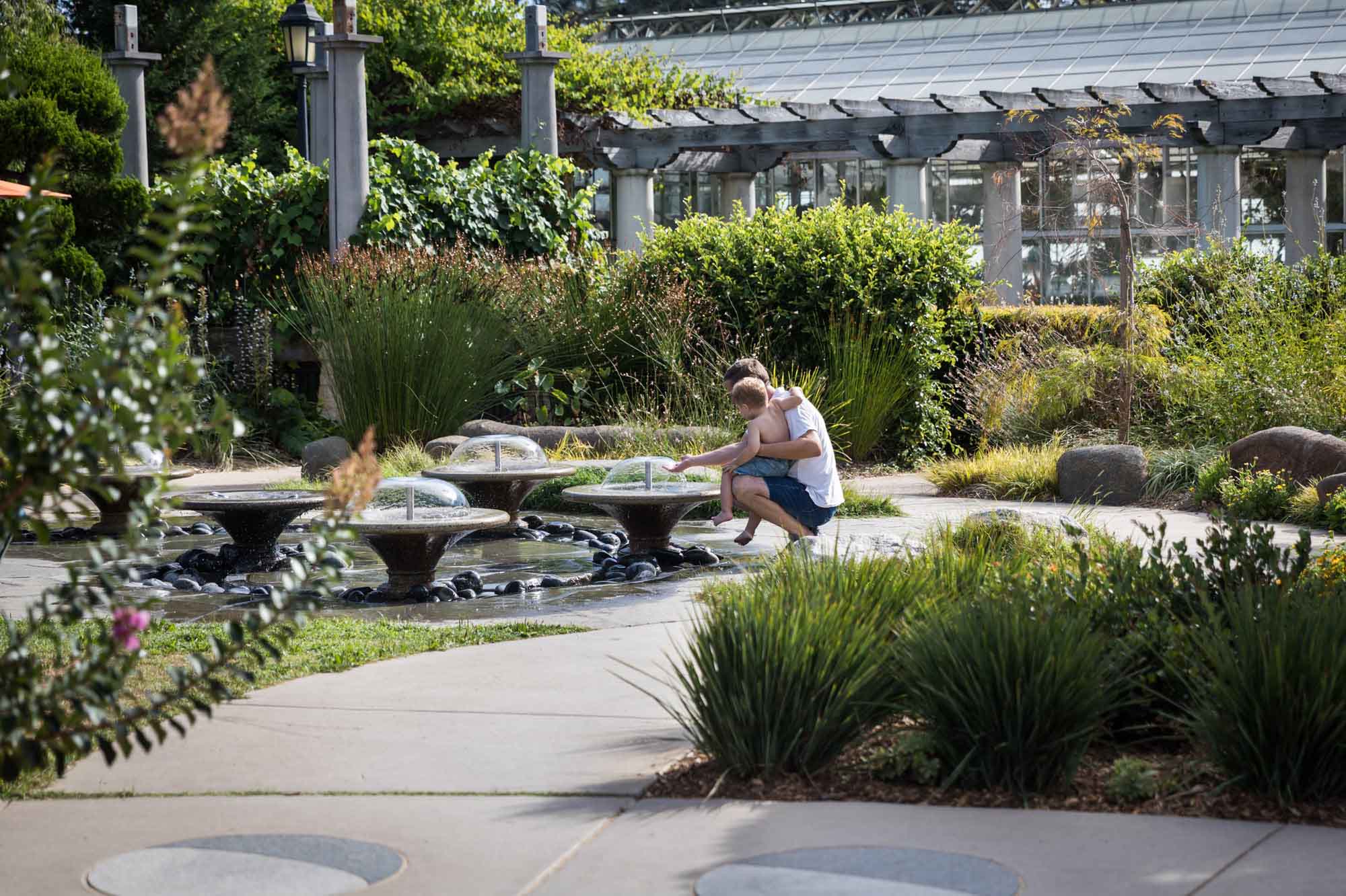 Father holding child in front of low fountains in the Children's Garden for a Huntington Gardens photo shoot guide article