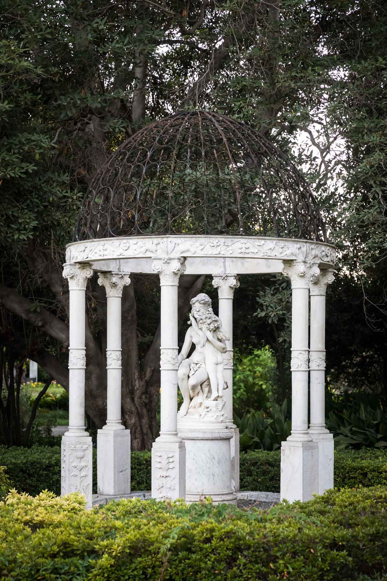 Stone gazebo structure surrounding stone classical sculpture in North Vista sculpture garden for a Huntington Gardens photo shoot guide article
