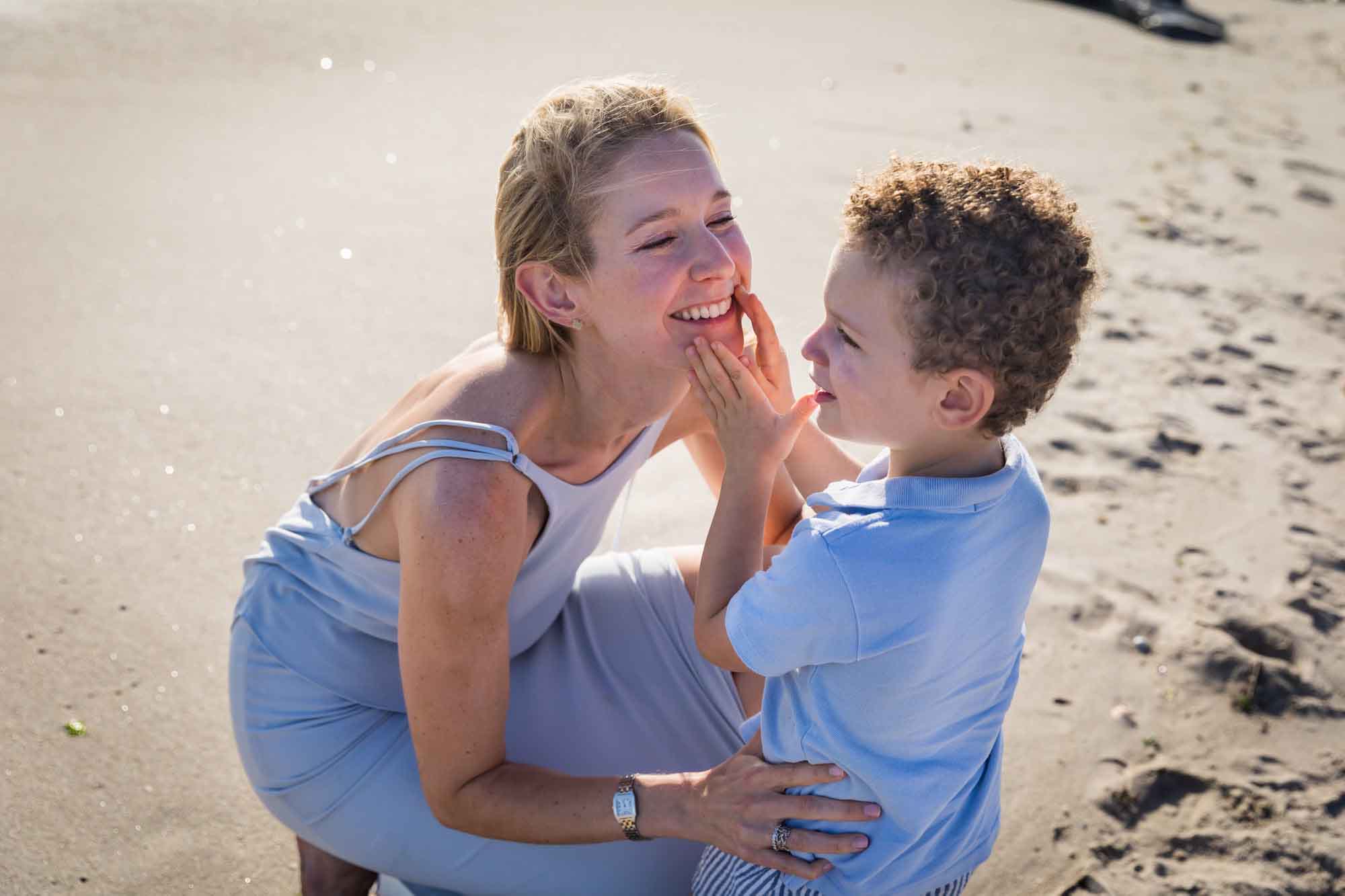 Mother crouched down looking at little boy with hands on mother's face at the beach for an article on La Jolla Cove family photos