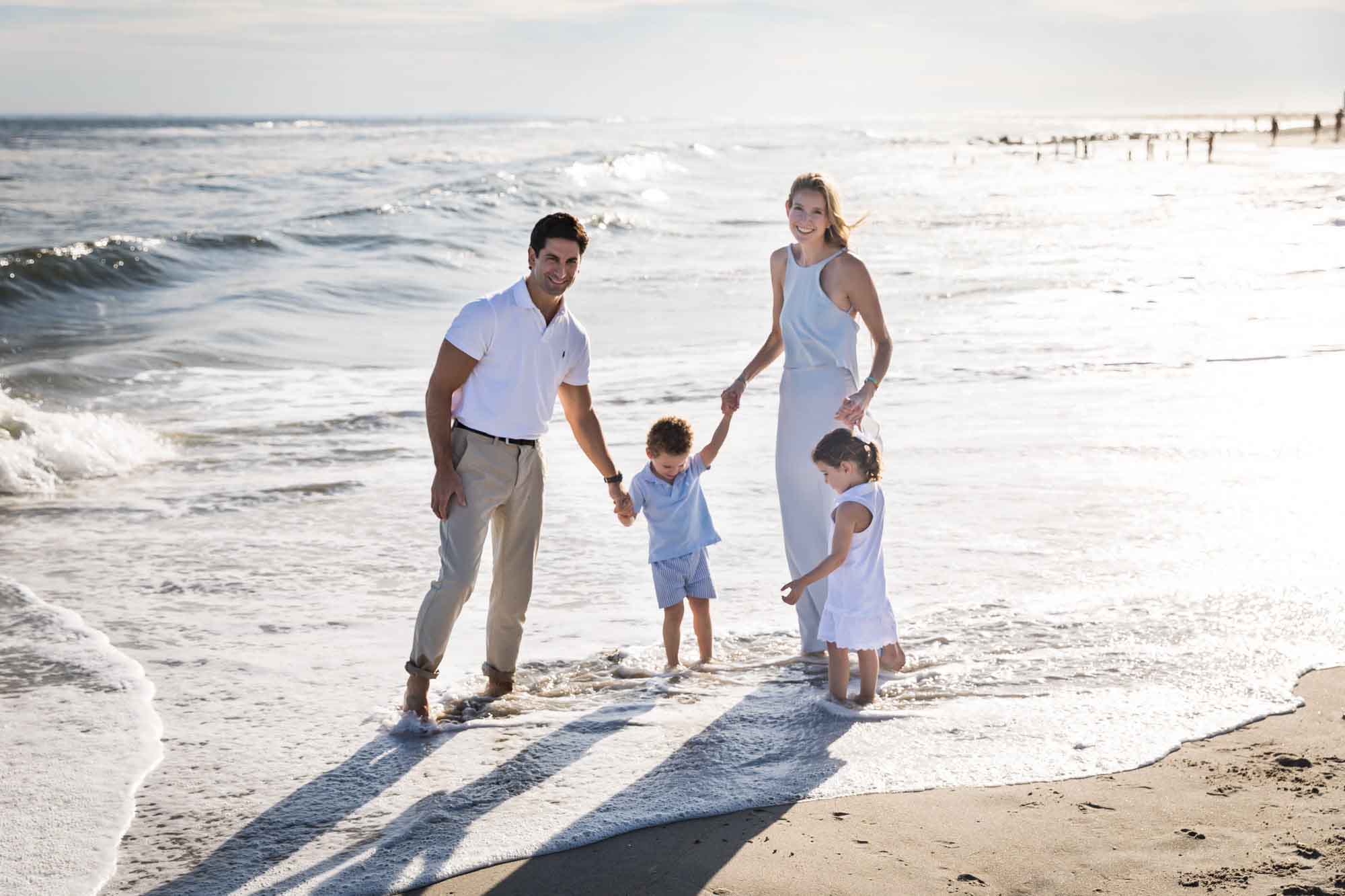 Mother and father holding hands with little boy and girl while standing in the surf at the beach for an article on La Jolla Cove family photos