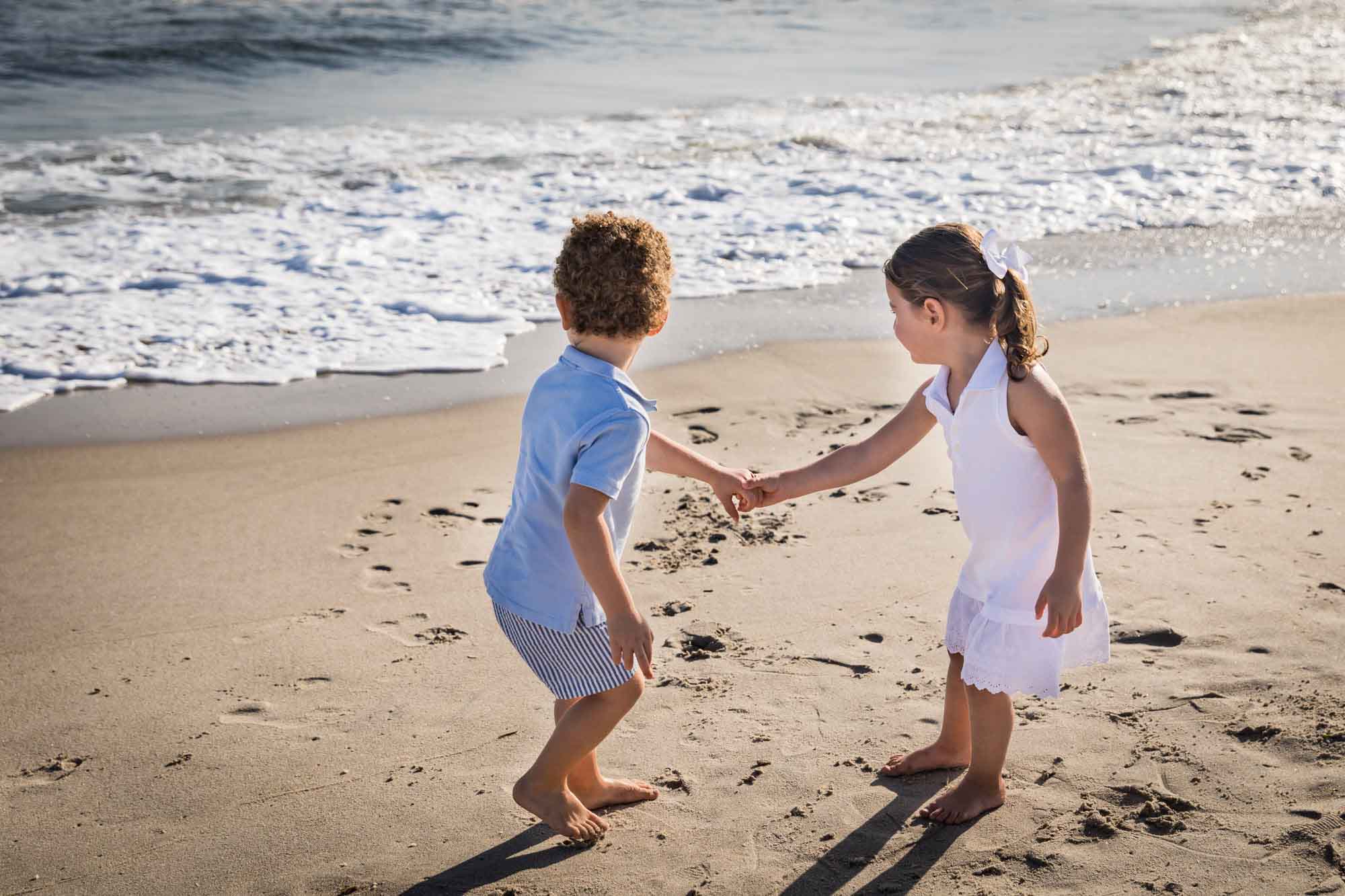 Little boy and girl holding hands standing in the sand looking back at the ocean for an article on La Jolla Cove family photos
