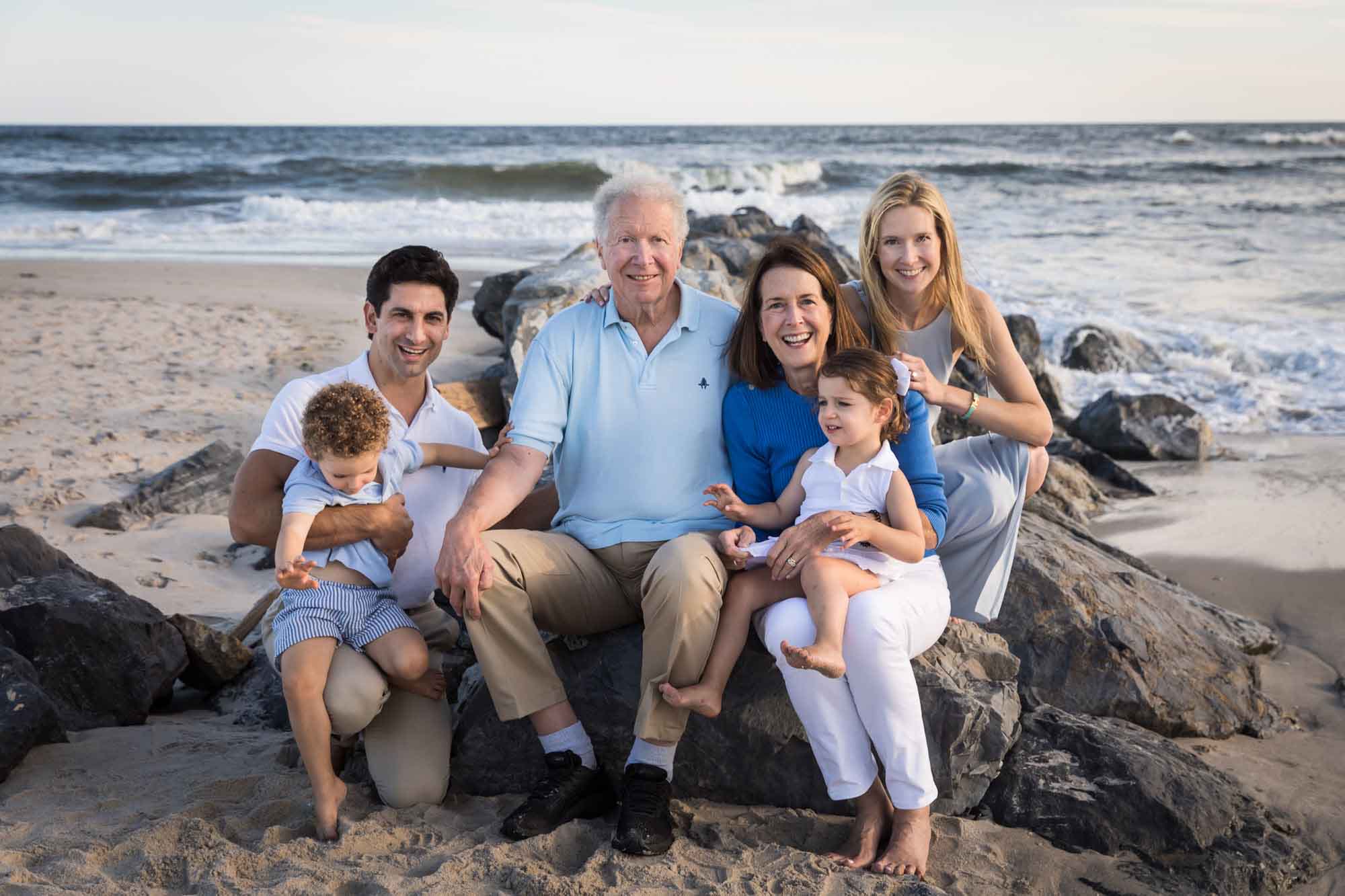 Grandparents, parents, and little boy and girl sitting on rocks in front of the ocean for an article on La Jolla Cove family photos