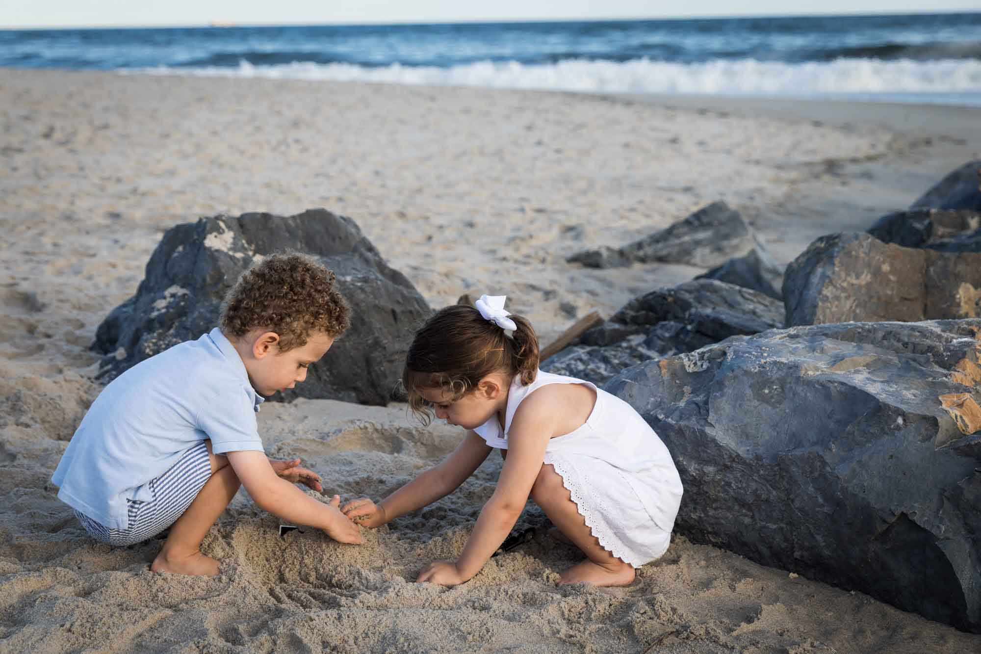 Little boy and girl digging in the sand in front of rocks and the ocean at the beach for an article on La Jolla Cove family photos