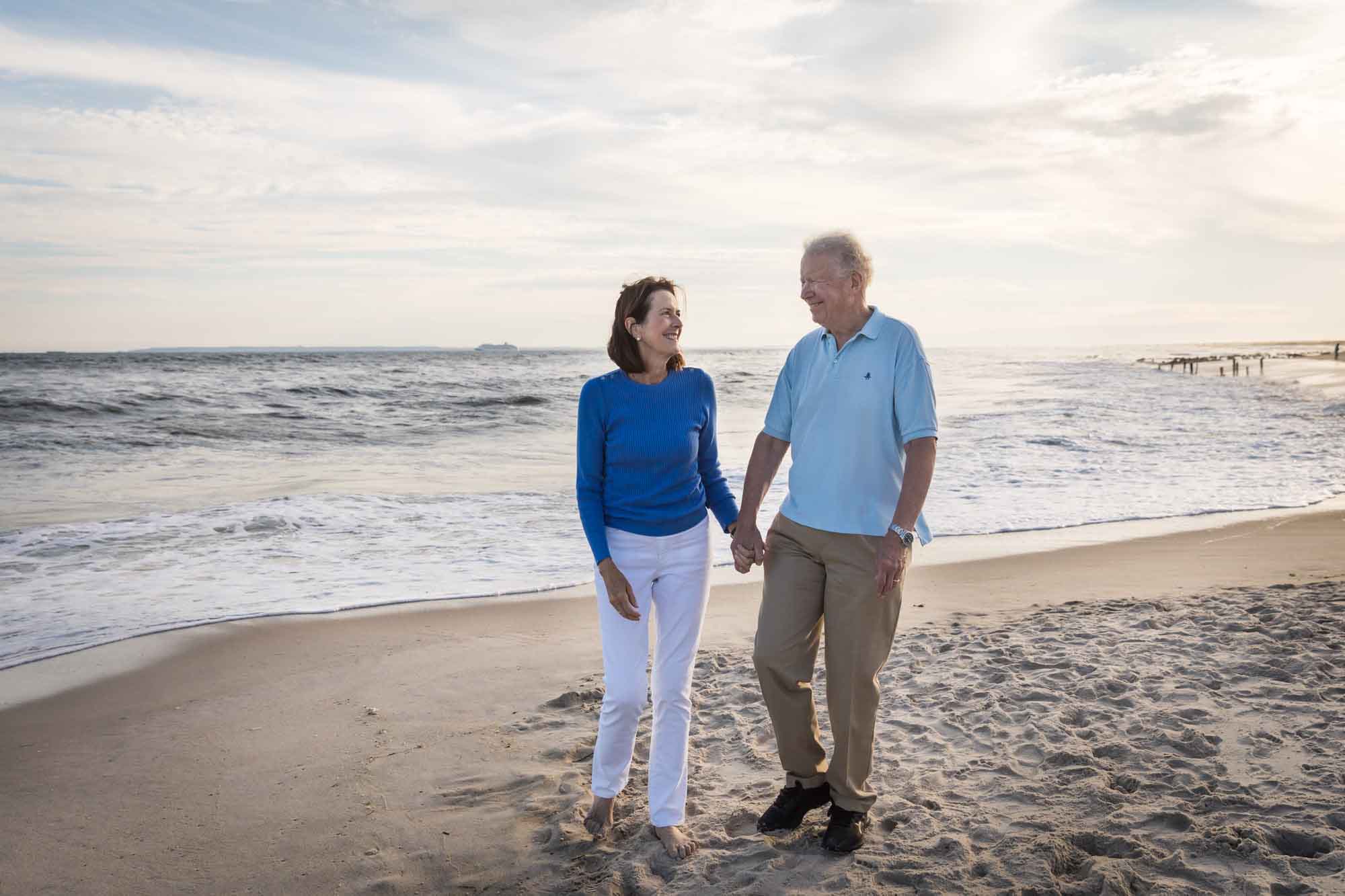 Older couple holding hands walking on beach in front of ocean for an article on La Jolla Cove family photos