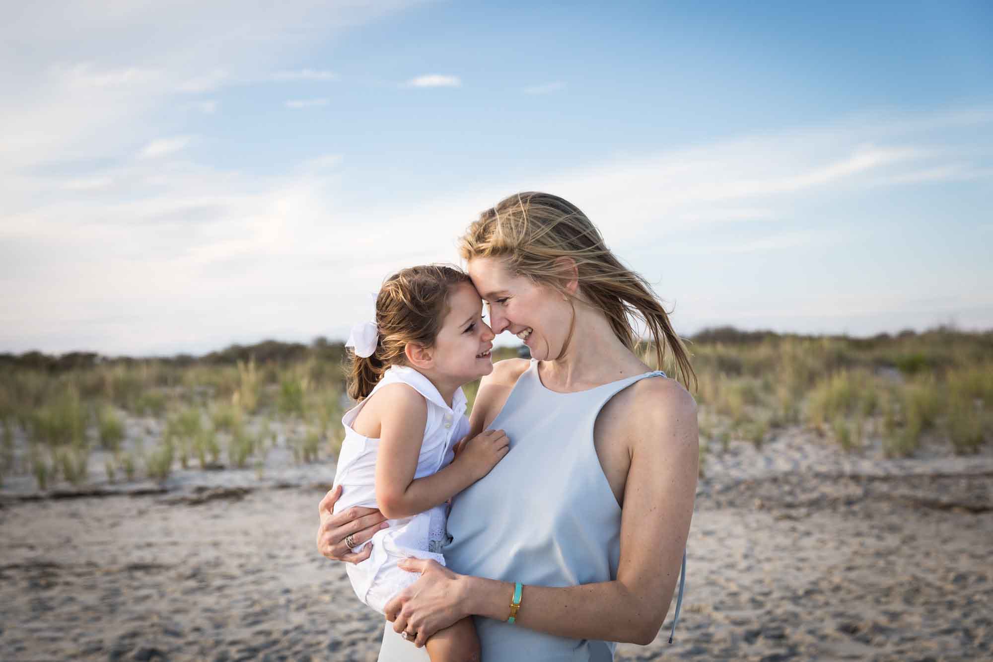 Mother holding little girl forehead to forehead in front of beach for an article on La Jolla Cove family photos