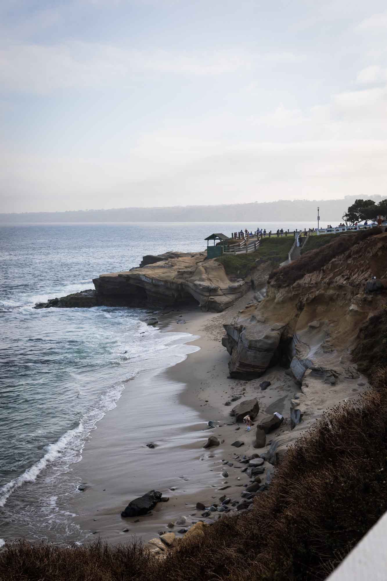 Beach with ocean and cliff embankments with pathway and railing leading down to beach for an article on La Jolla Cove family photos