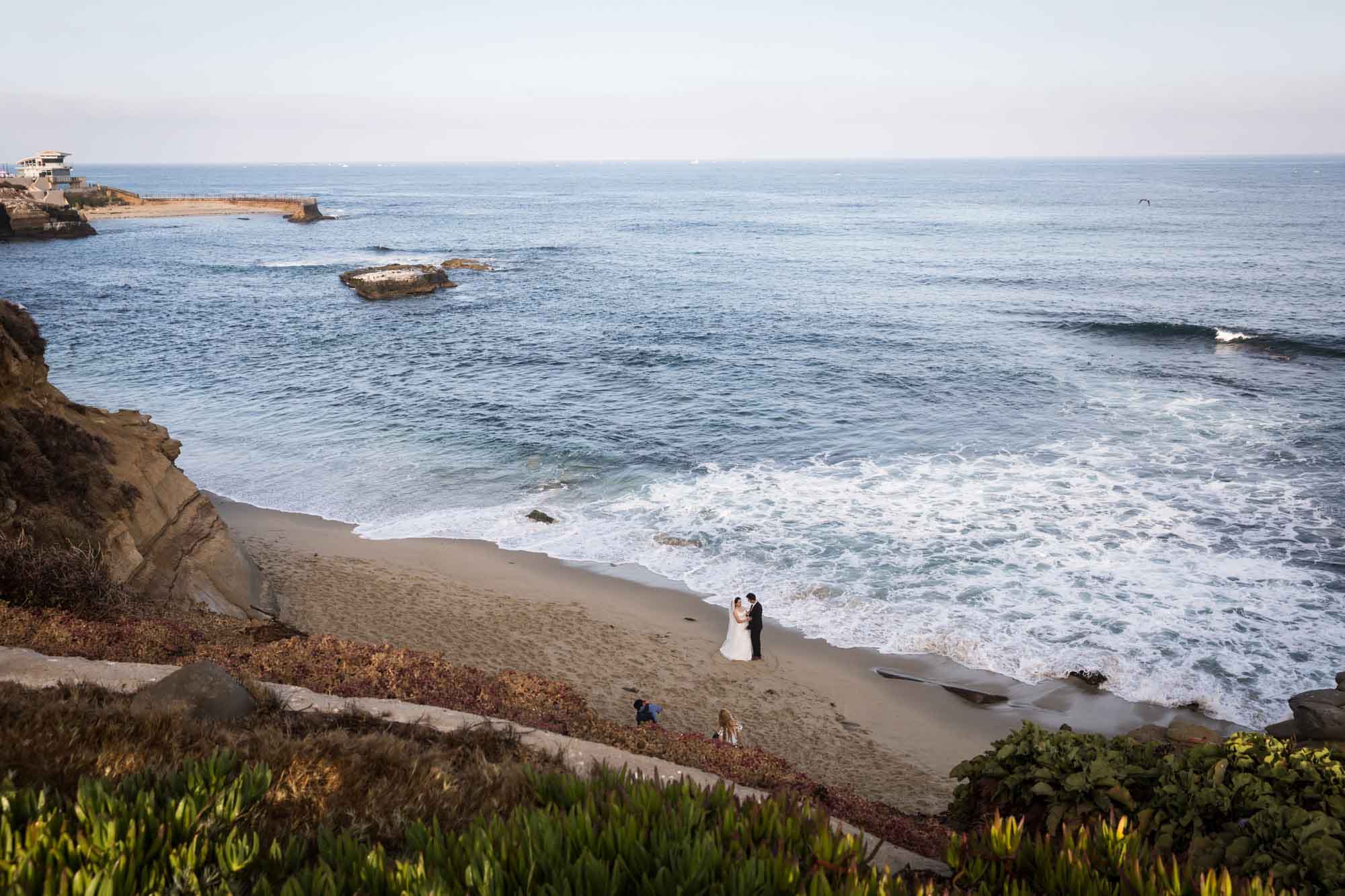 Bride and groom taking photos with photographer at Shell Beach for an article on La Jolla Cove family photos