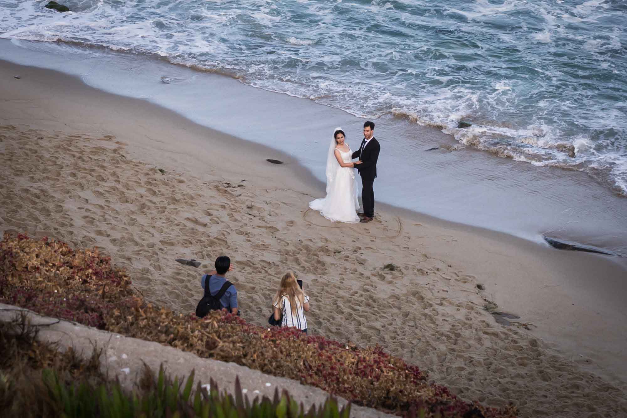Bride and groom taking photos with photographer at Shell Beach for an article on La Jolla Cove family photos