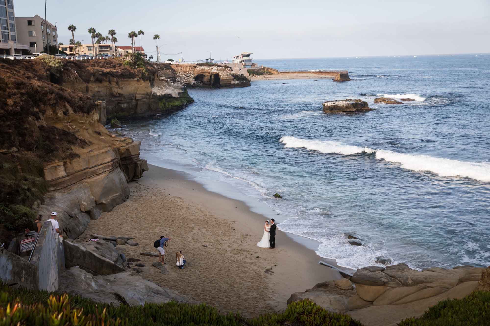 Bride and groom taking photos with photographer at Shell Beach for an article on La Jolla Cove family photos