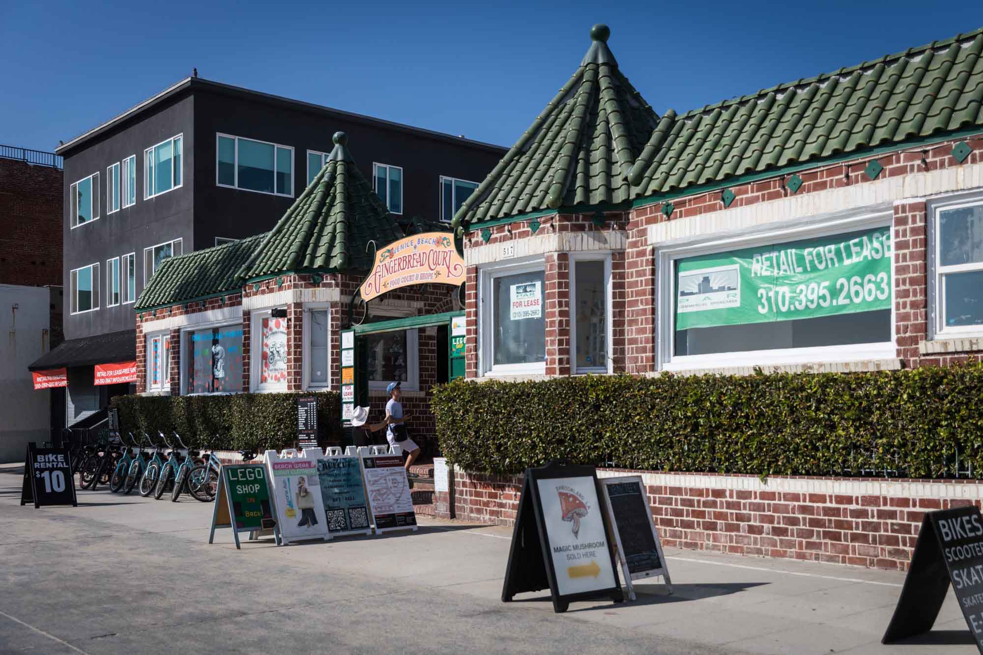 The front of the Gingerbread Court showing a large 'Retail for Lease' sign in green and several retail sandwich board signs for an article on Venice Canals engagement photos