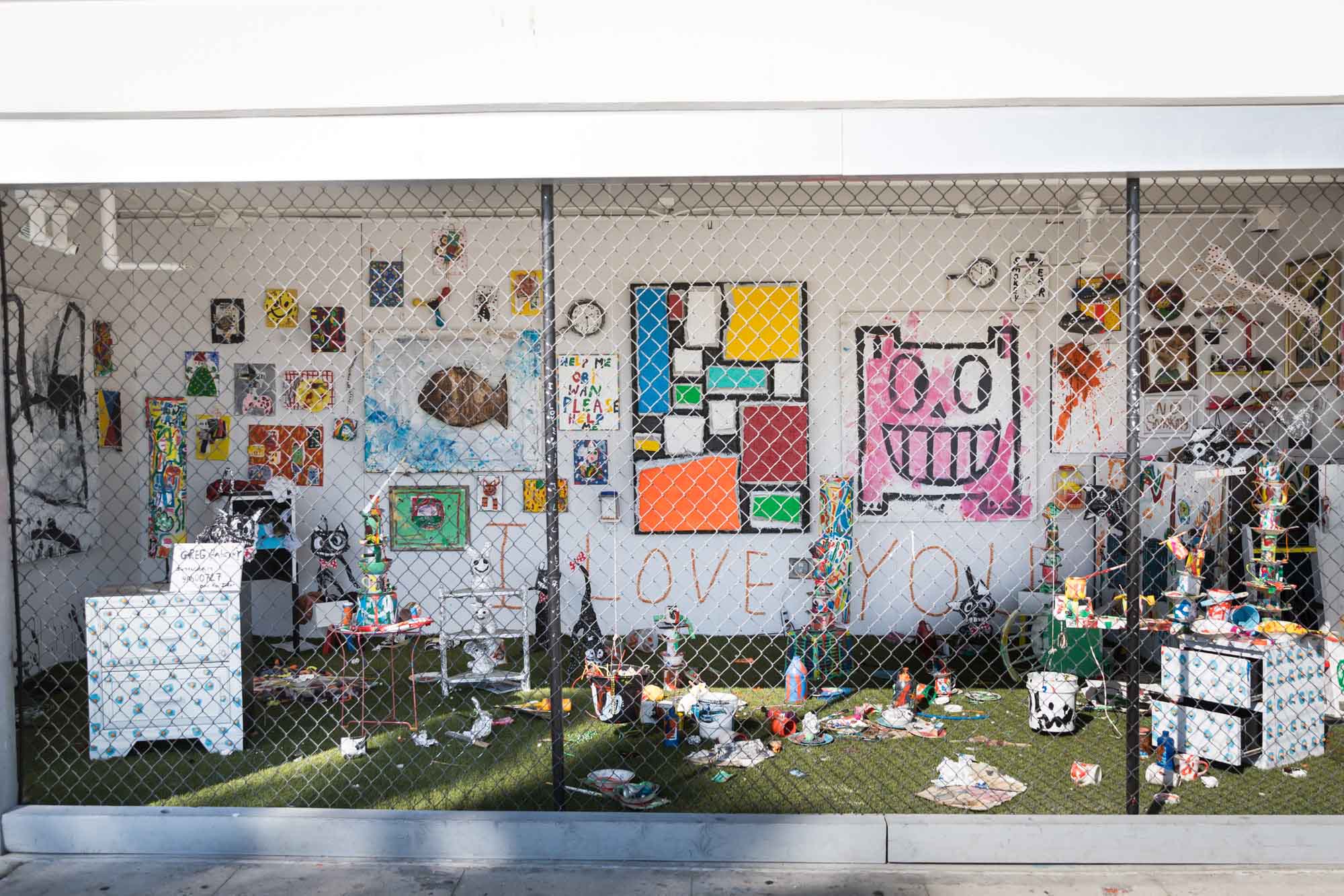 A colorful art exhibit of items with drawers and trash behind a black fence in Venice Beach for an article on Venice Canals engagement photos
