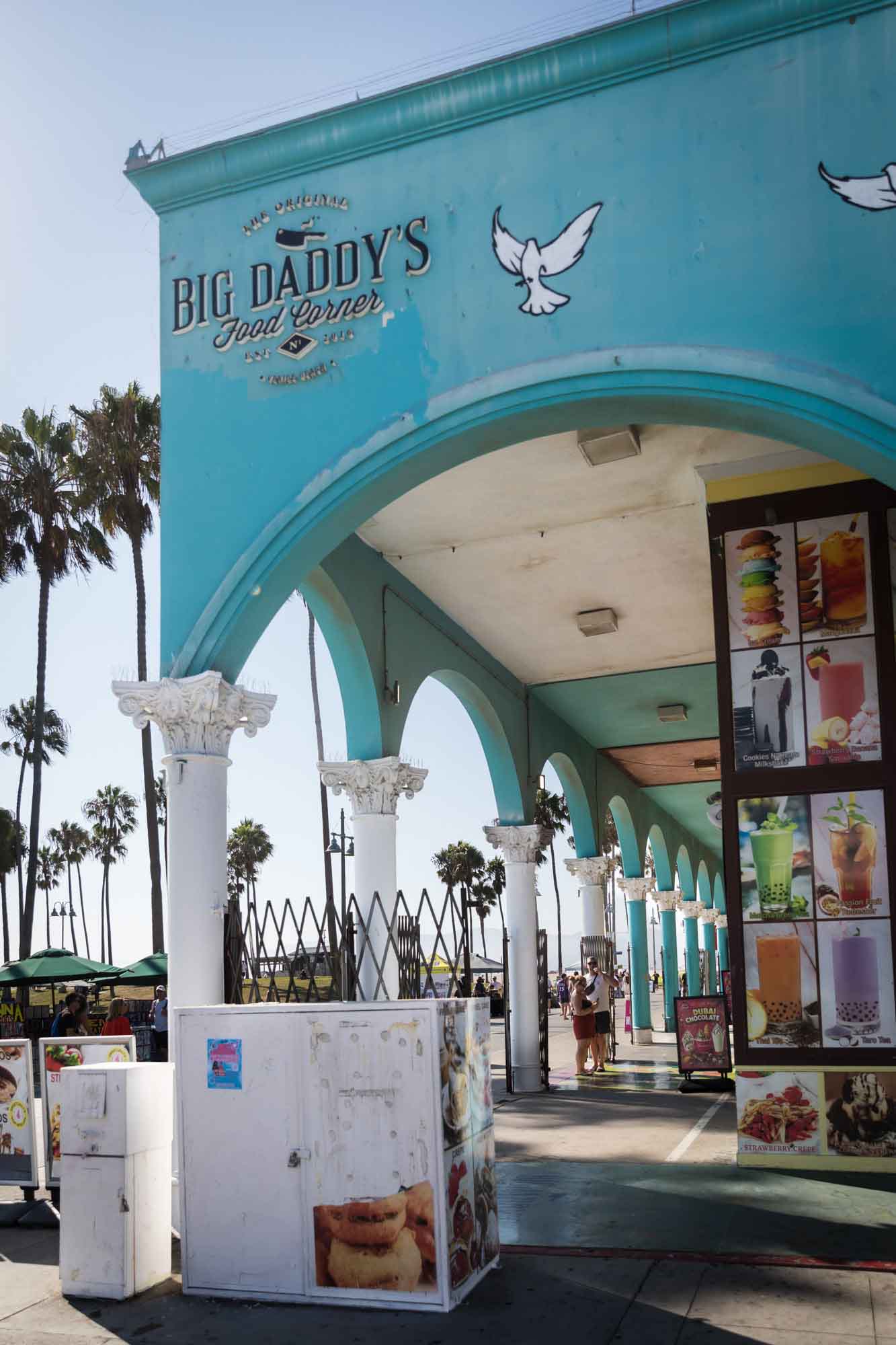 Aqua exterior colonnade of the Venice Market on Venice Beach with palm trees in the background for an article on Venice Canals engagement photos